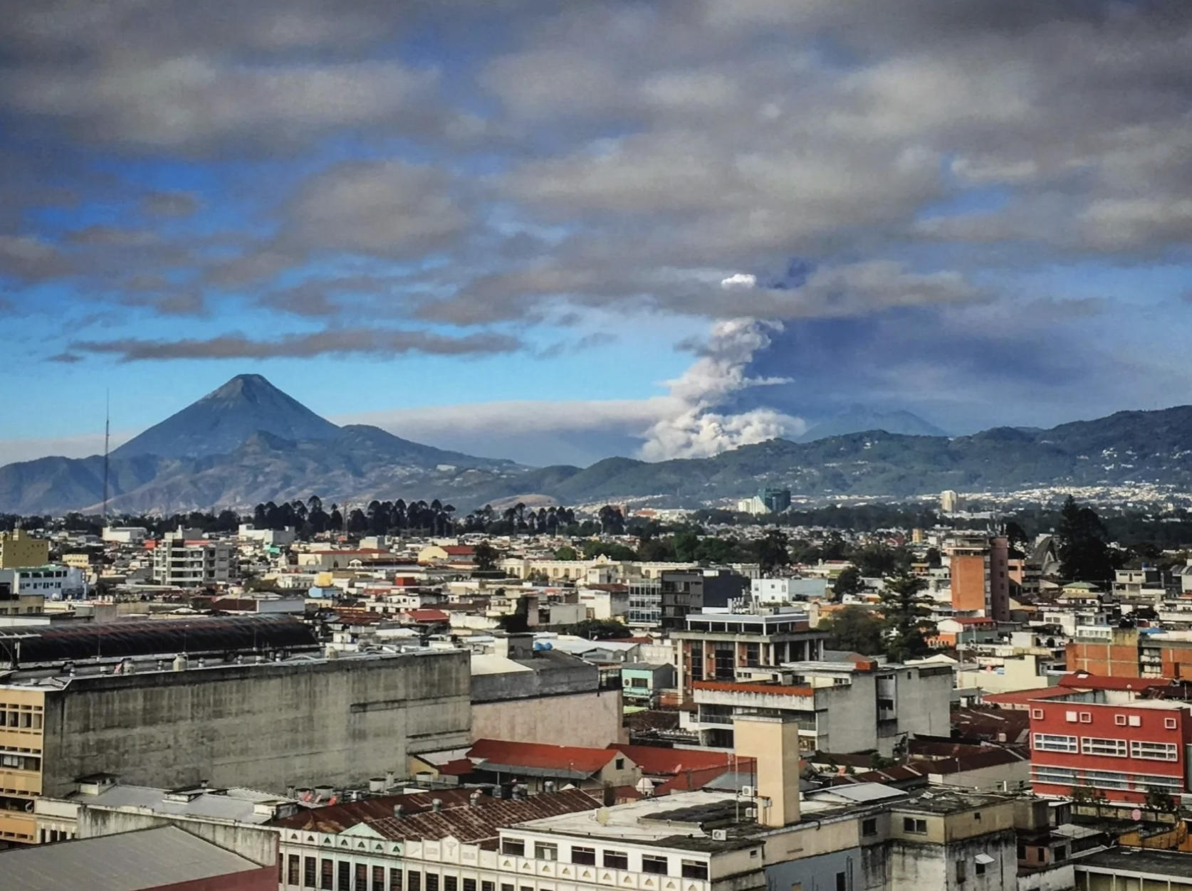 Warm Guatemala weather with a volcano is puffing smoke into the air beyond the cityscape