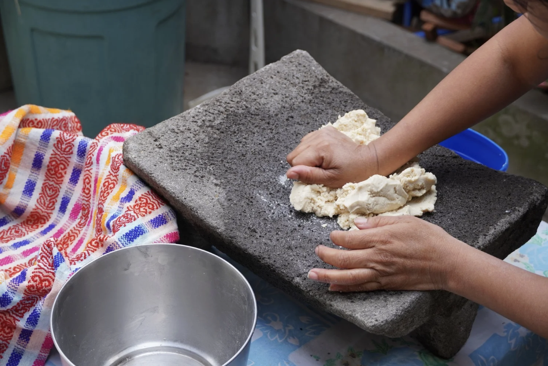 Hands are pounding masa on a stone in Guatemala while making tortillas, a vegan food in Guatemala Hands are pounding masa on a stone in Guatemala while making tortillas, a vegan food in Guatemala