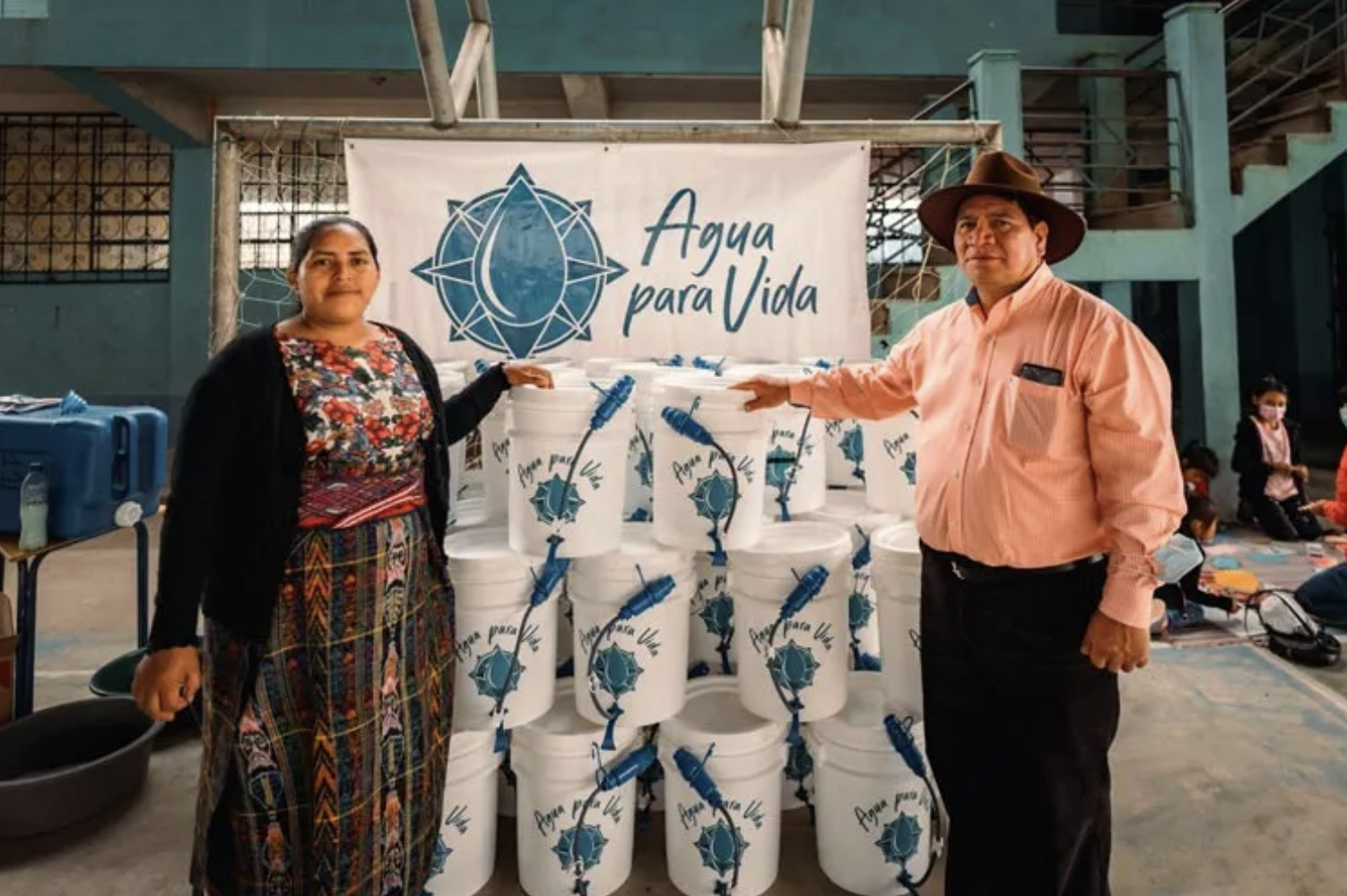 Two Guatemalan people are standing with buckets showcasing the Water For Life program