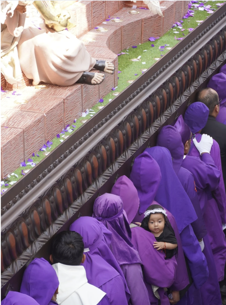 Guatemalans wearing purple are carrying a float during Semana Santa