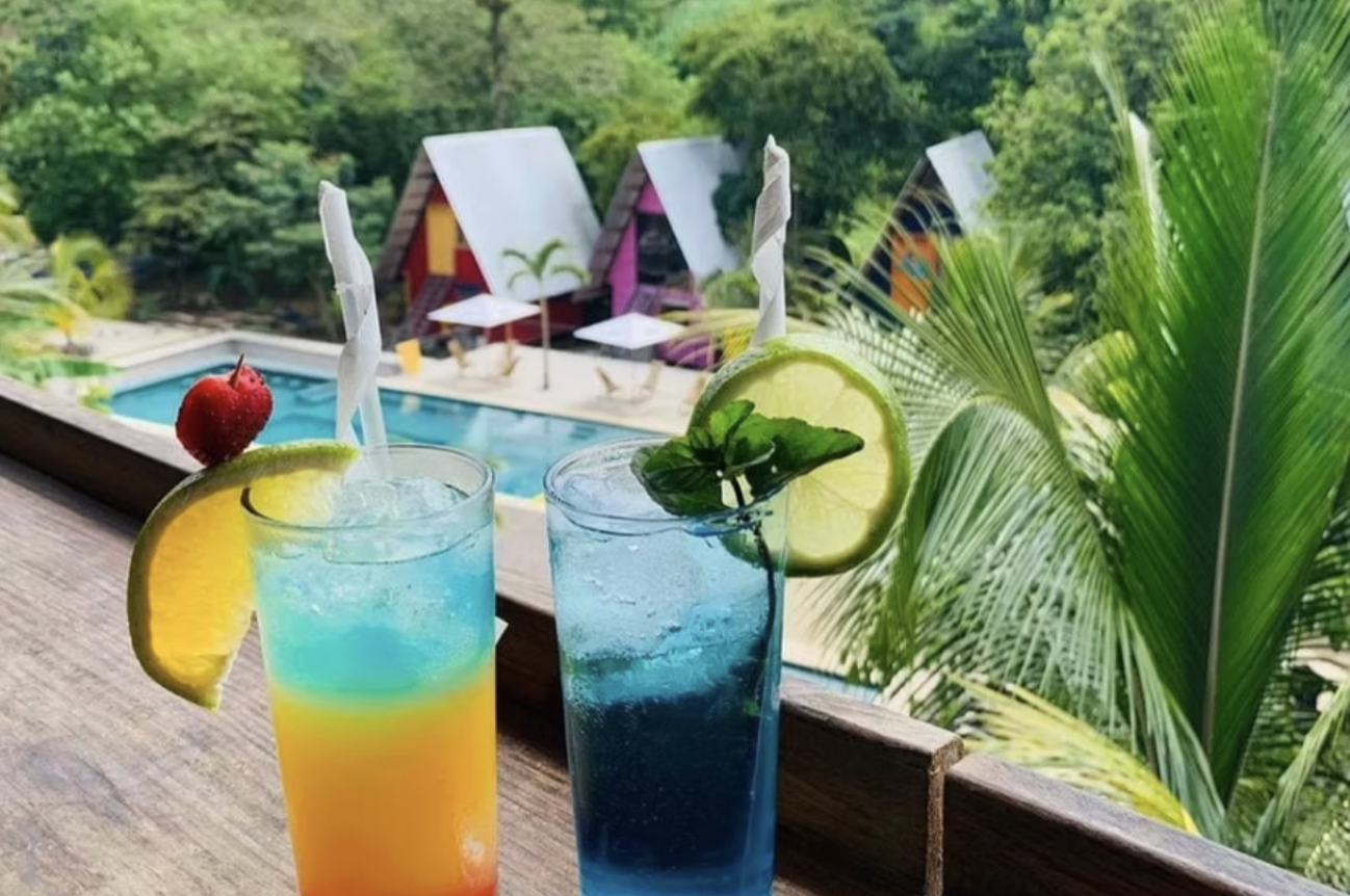 Two tropical drinks are sitting on a bench above the pool at a hotel in Semuc Champey 