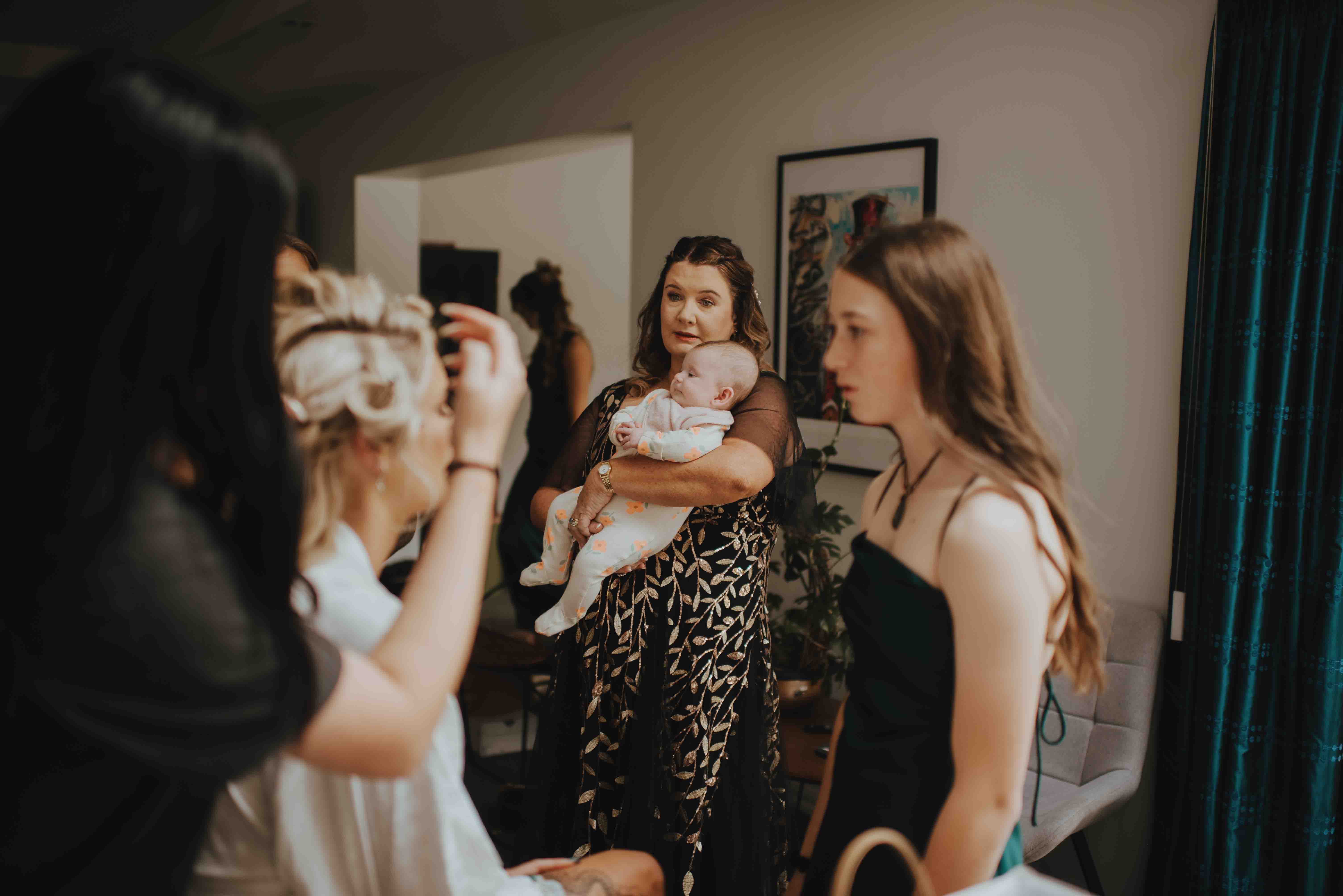 mother of the bride holding bride's baby niece watching her get ready