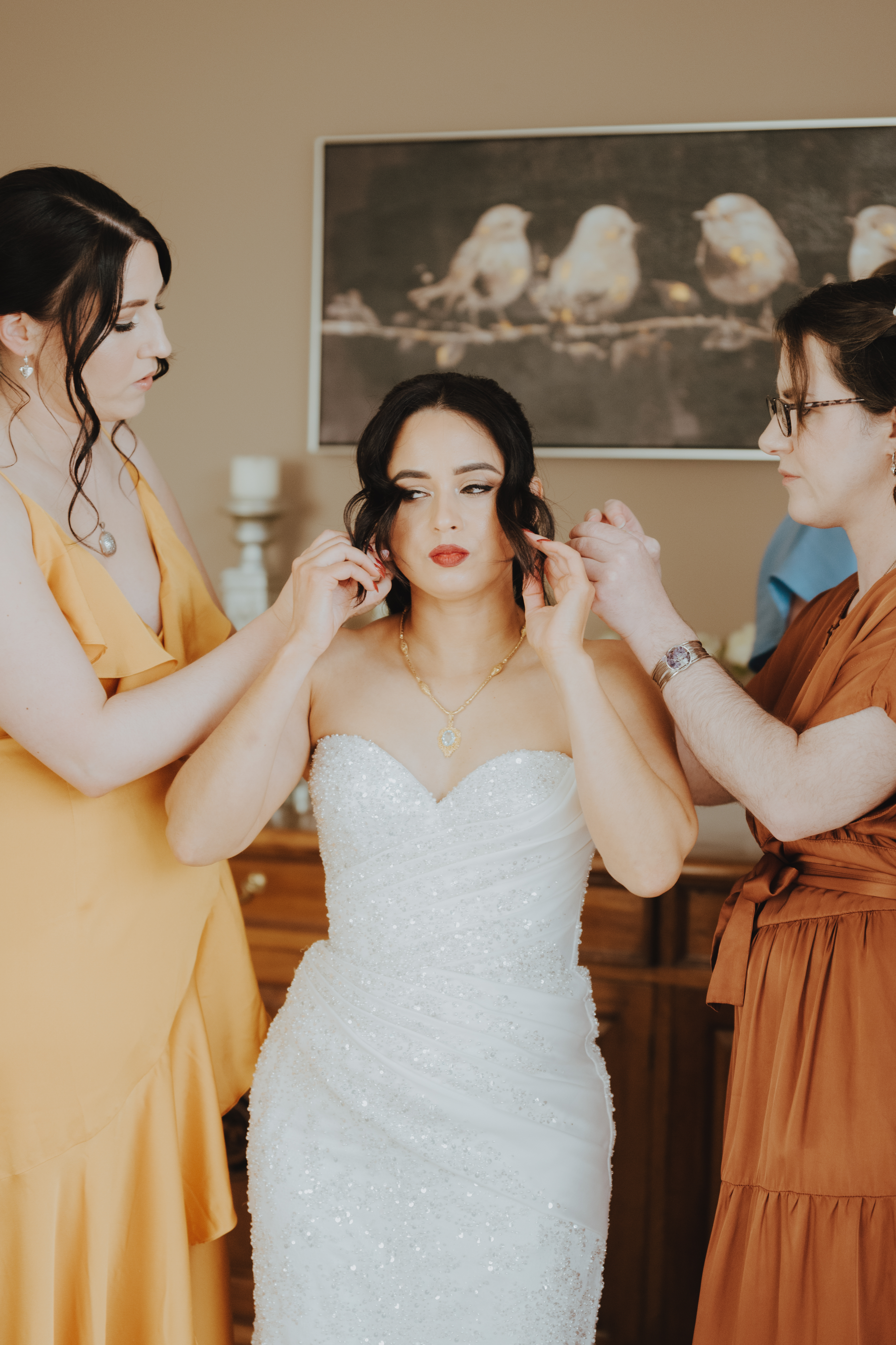 bride putting in her earrings while bridesmaids fluff the dress bride putting in her earrings while bridesmaids fluff the dress