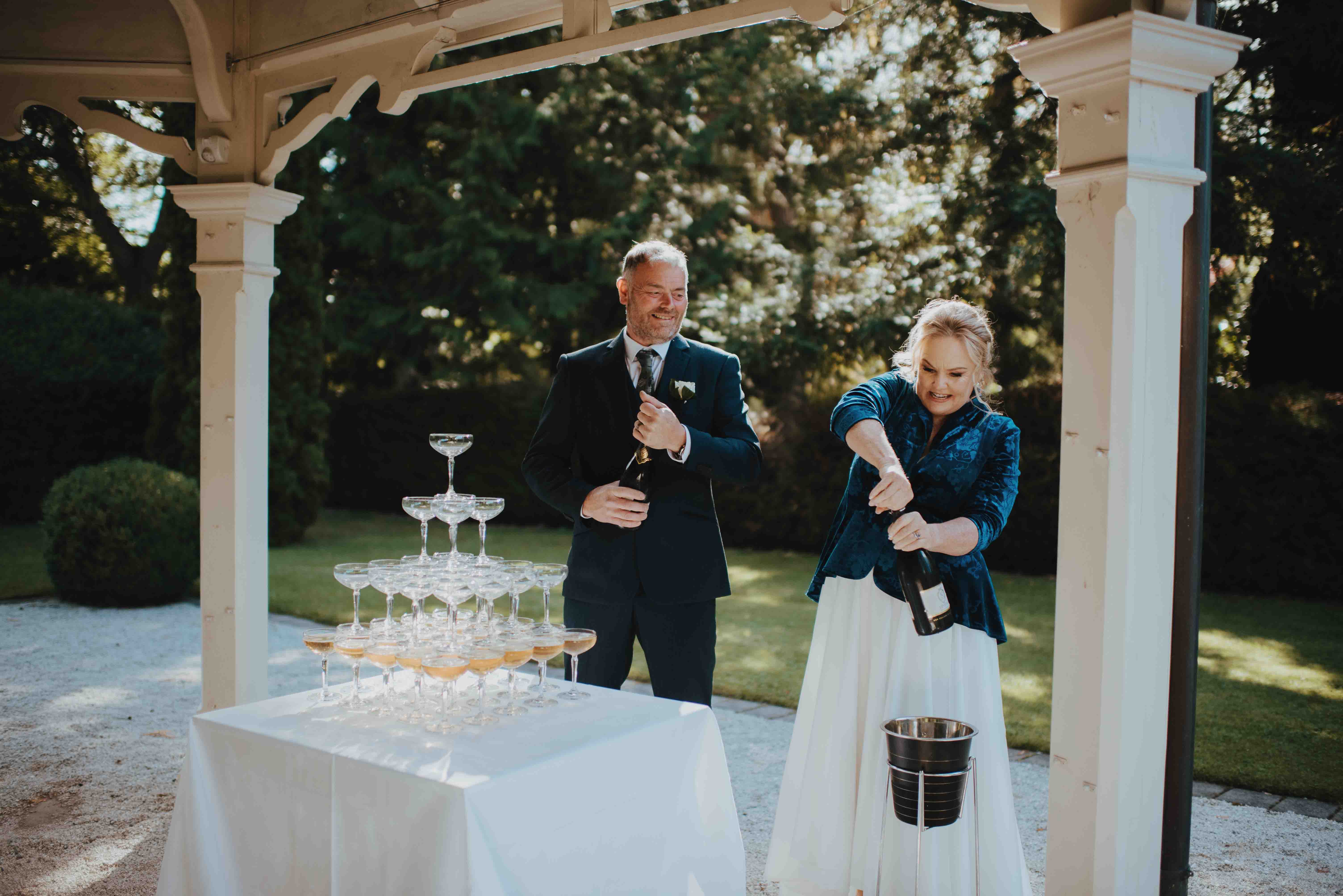 bride stubbornly trying to undo a cork on a bottle for the champagne tower while her new husband giggles
