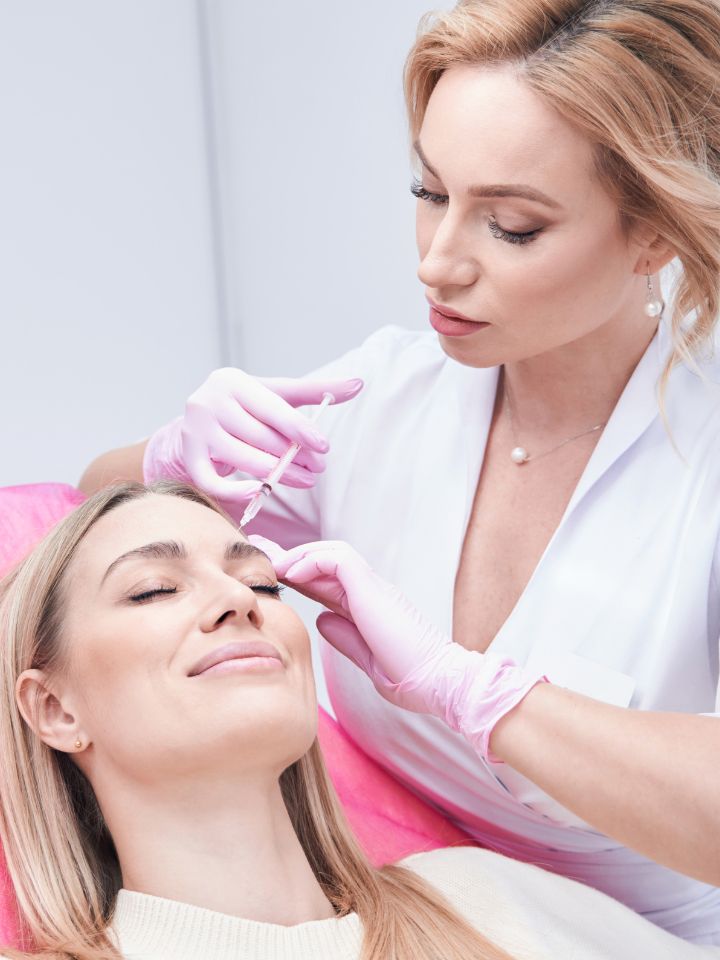 A professional administering a dermal filler injection to a client’s face in a clinical setting.