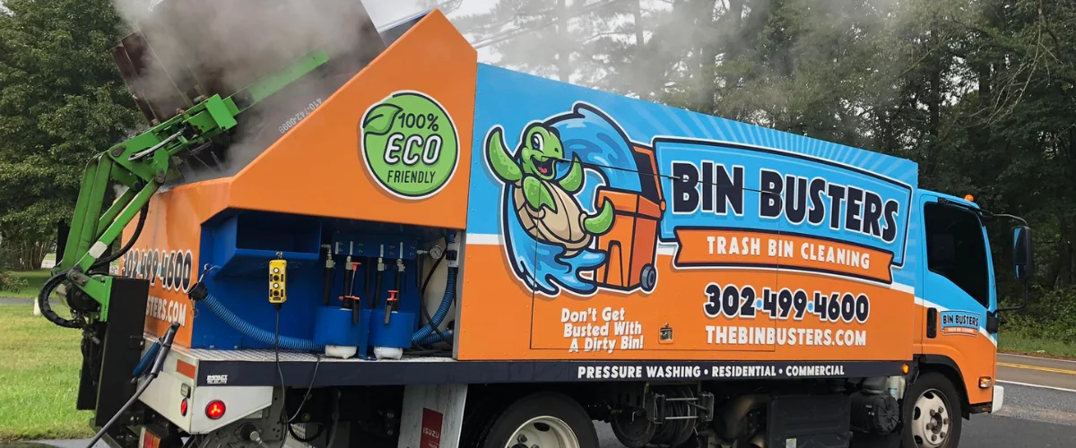 A Bin Busters truck with "100% ECO FRIENDLY" logo and a turtle mascot, cleaning a bin with steam. A Bin Busters truck with "100% ECO FRIENDLY" logo and a turtle mascot, cleaning a bin with steam.