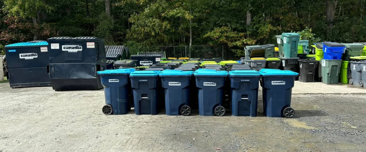 A wide view of a Casella yard filled with various sizes of blue, green, and black recycling bins and dumpsters. A wide view of a Casella yard filled with various sizes of blue, green, and black recycling bins and dumpsters.