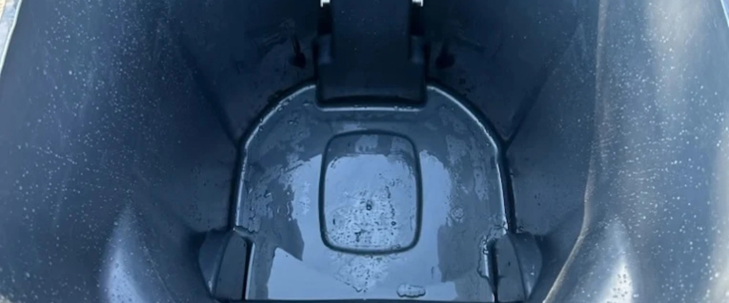 A top-down view inside a dark wet bin or container, showing water droplets on the sides and accumulated water at the bottom. A top-down view inside a dark wet bin or container, showing water droplets on the sides and accumulated water at the bottom.