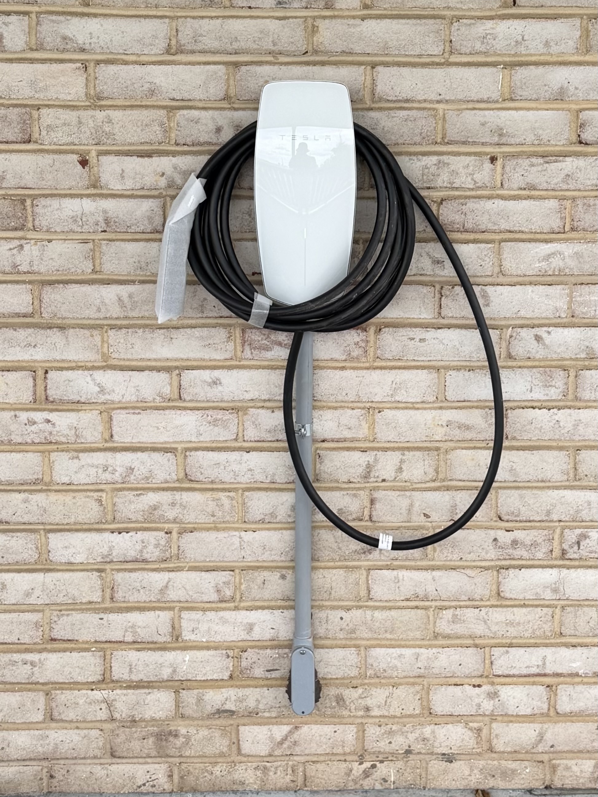 Level 2 EV charger mounted on a brick exterior wall with conduit run down to the panel