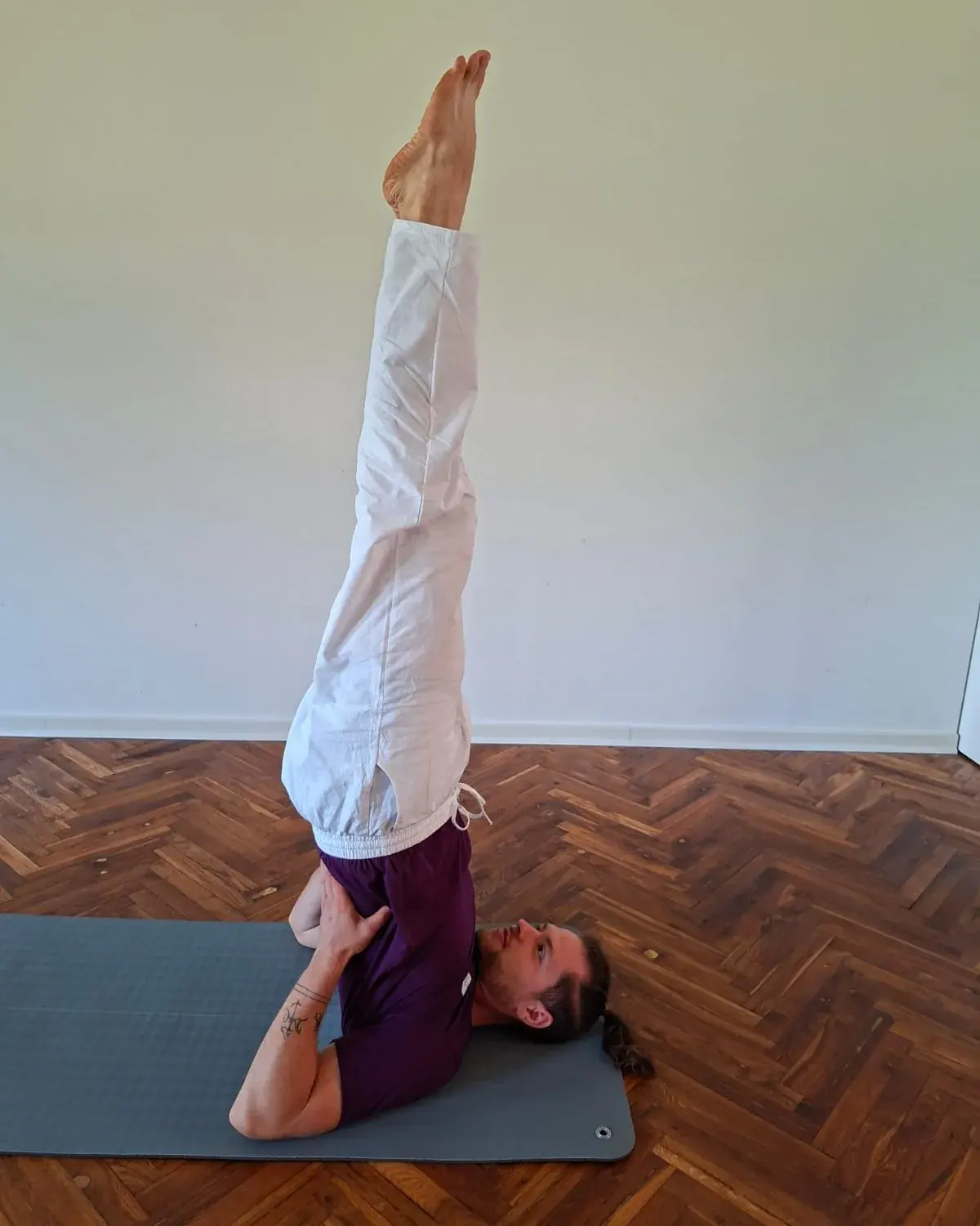 Aurimas Savickas in a supported shoulder stand (Salamba Sarvangasana) on a yoga mat