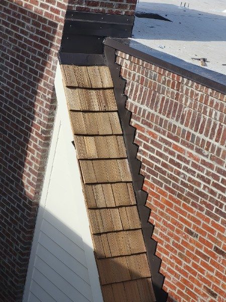 Cedar shake and custom metal flashing at a brick chimney wall