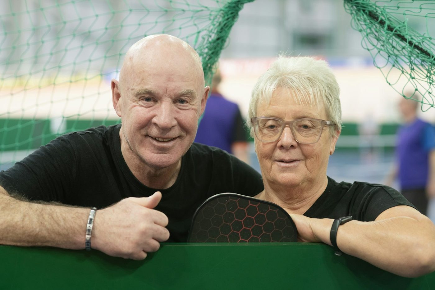 Smiling couple holding pickleball paddles at the net