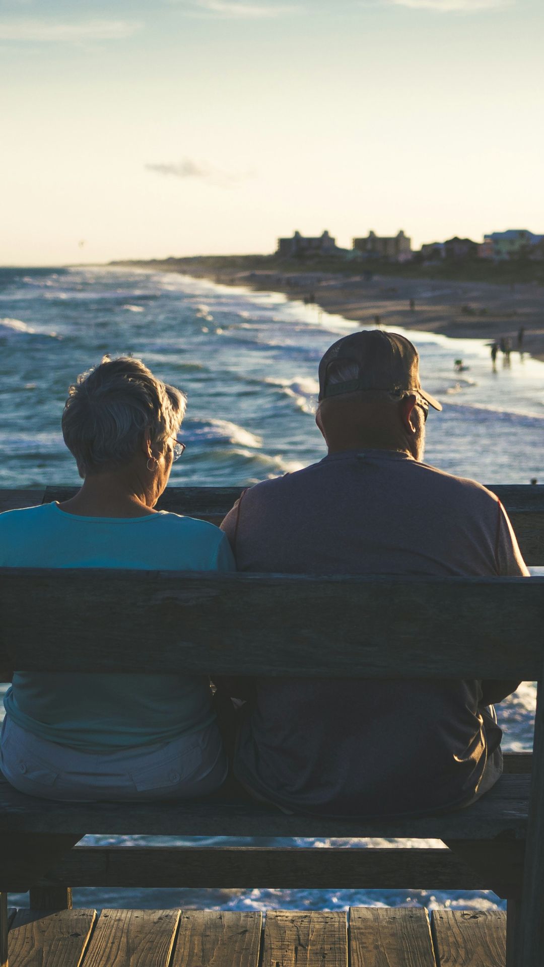 older couple sitting on a bench staring at the ocean