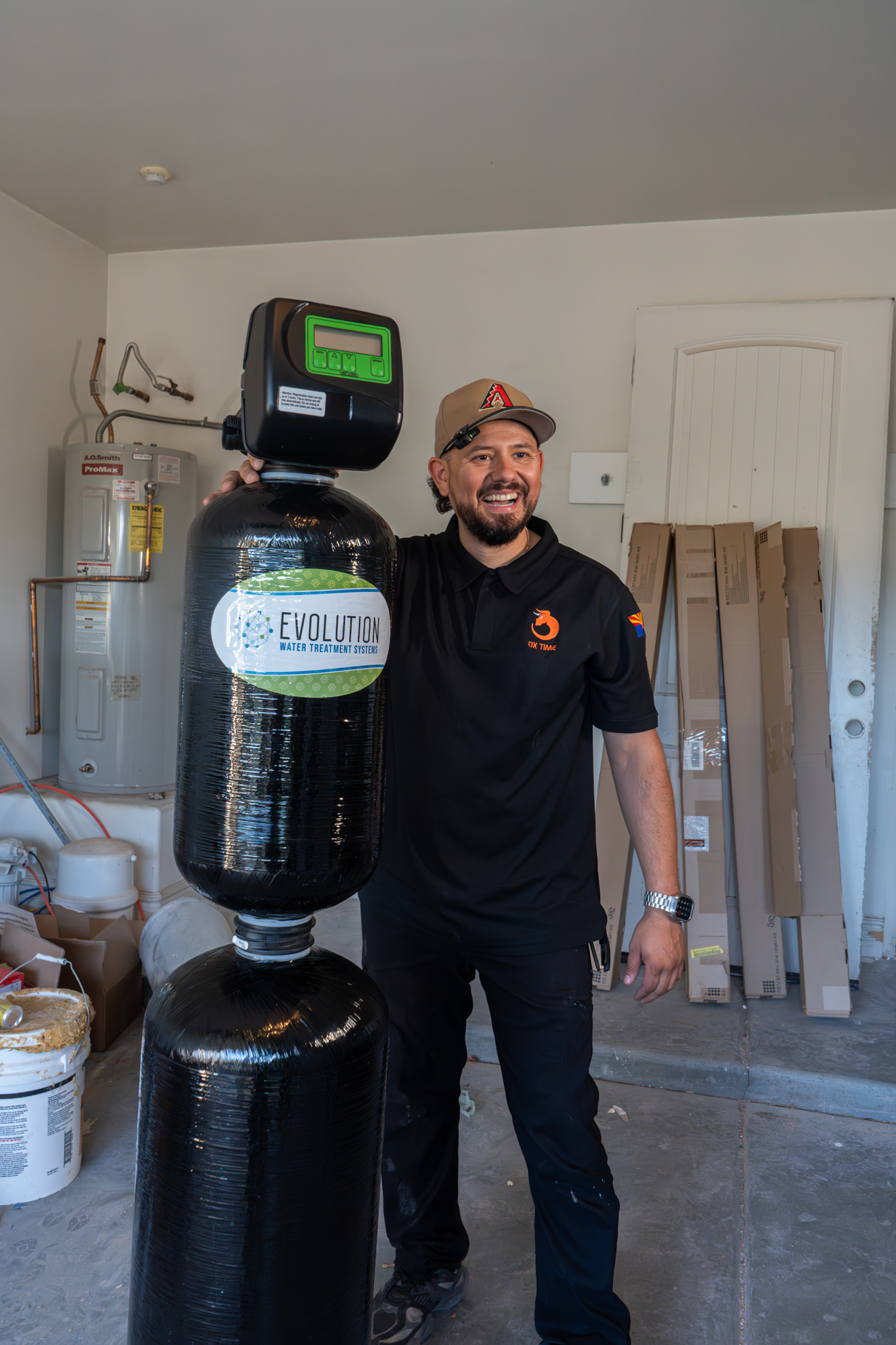 Erik Caballero, Owner of OX Plumbing, standing next to a water softener system