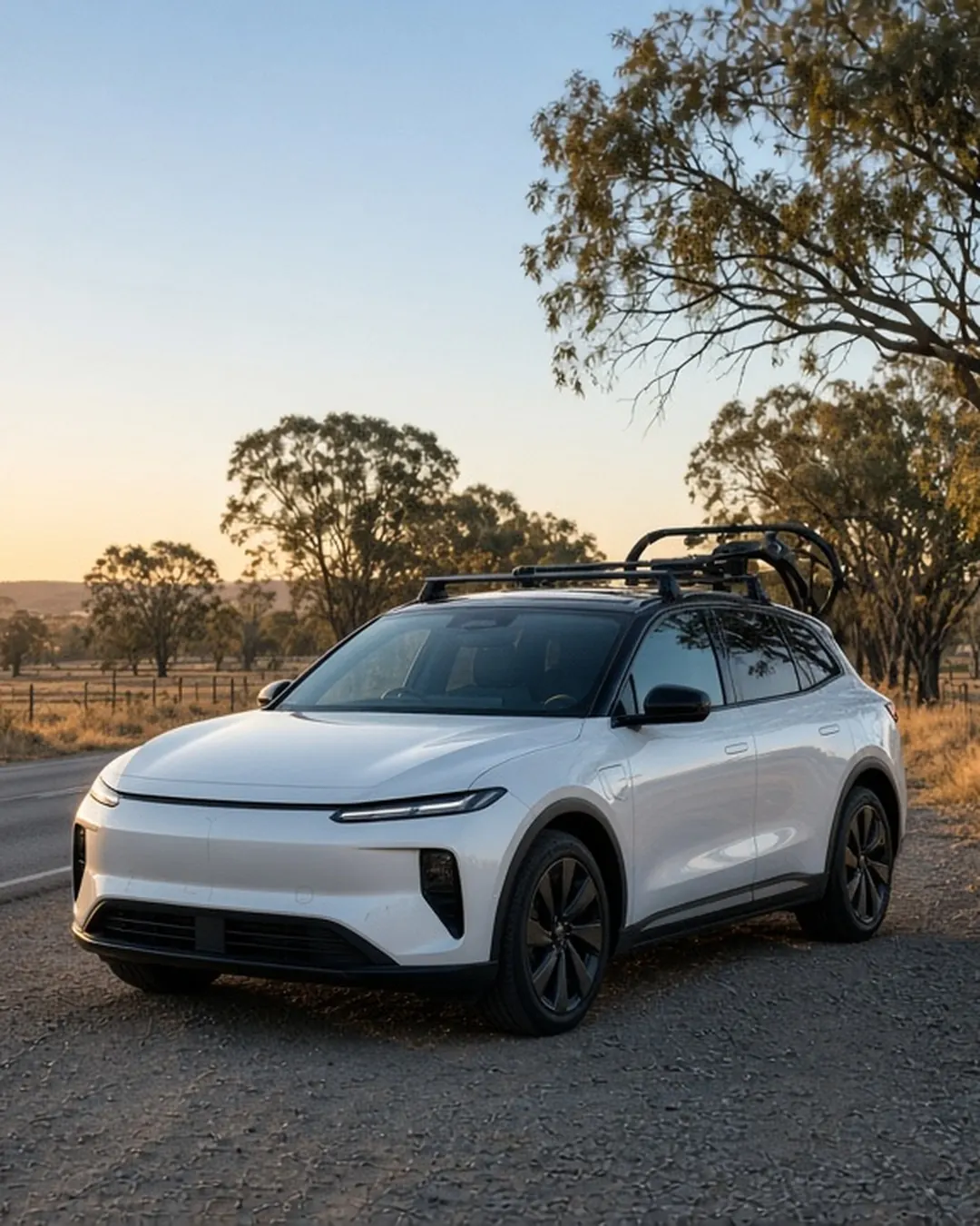 White electric SUV with roof racks and a bike carrier on a country road