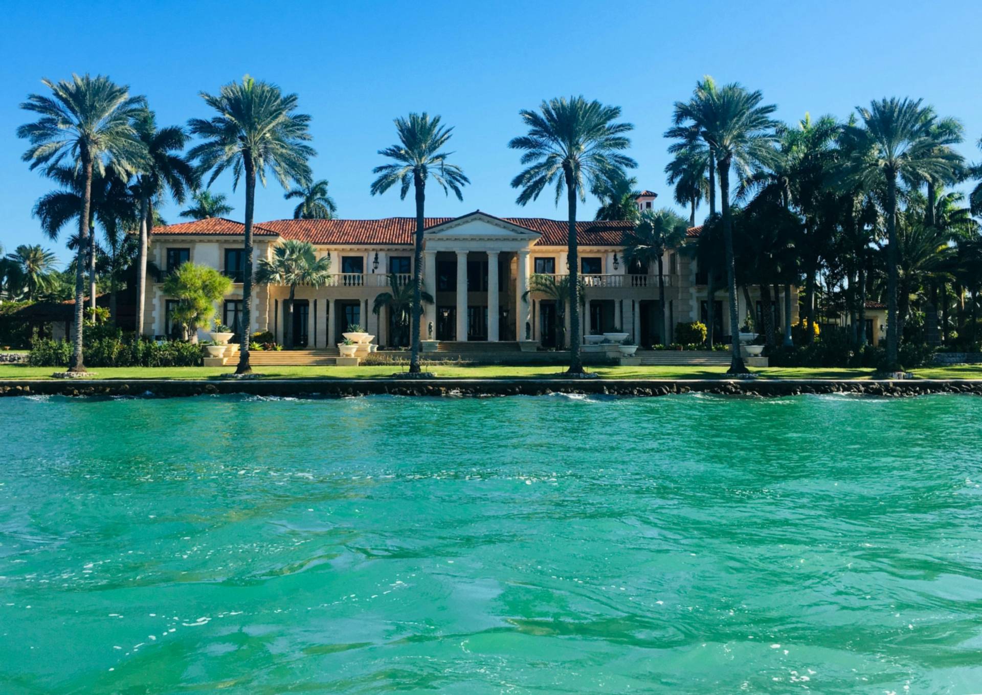Waterfront home with palm trees above turquoise water