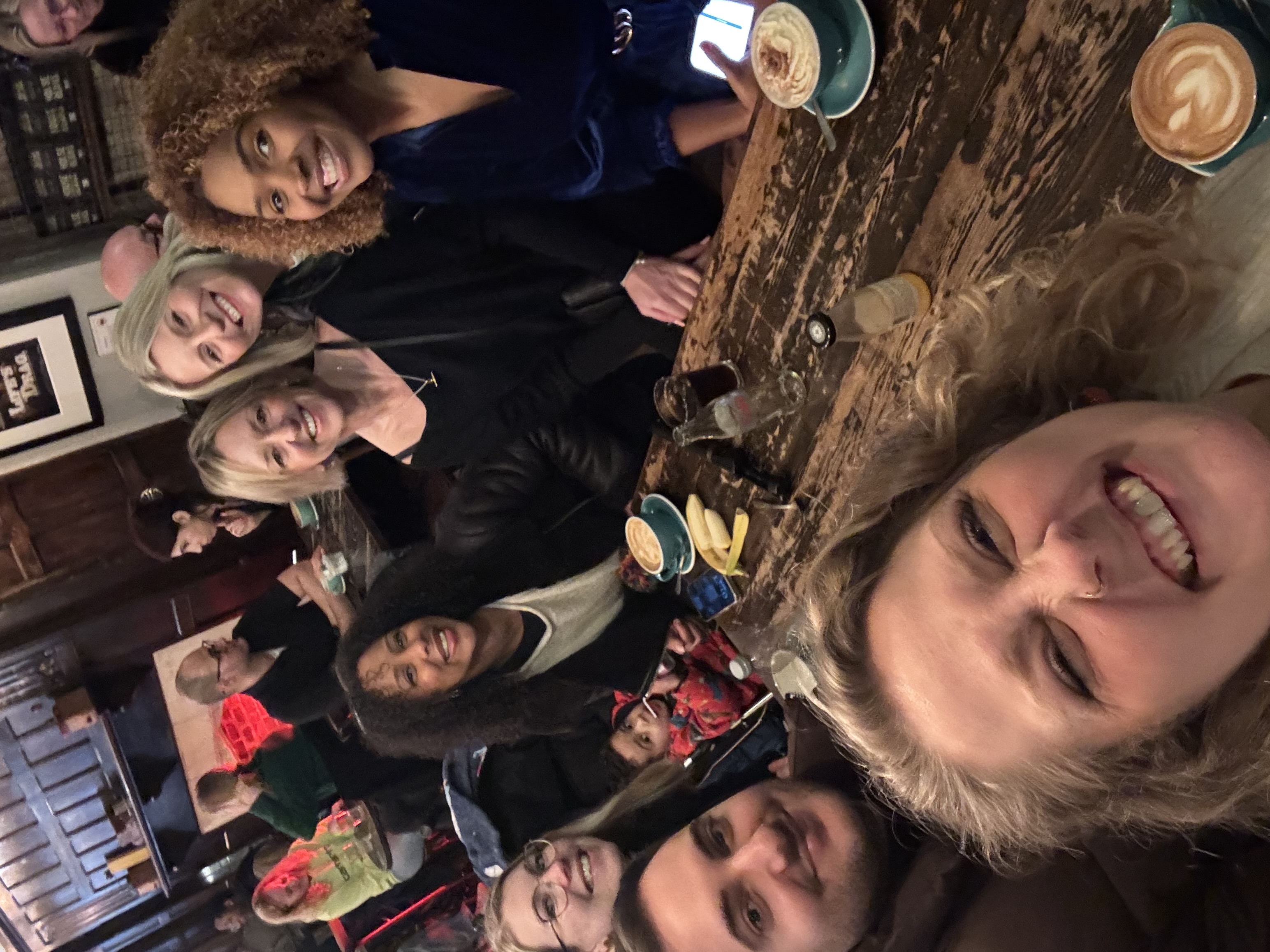 Group of people snuggled in a coffee shop, taking a selfie style photo, smiling at the camera Group of people snuggled in a coffee shop, taking a selfie style photo, smiling at the camera