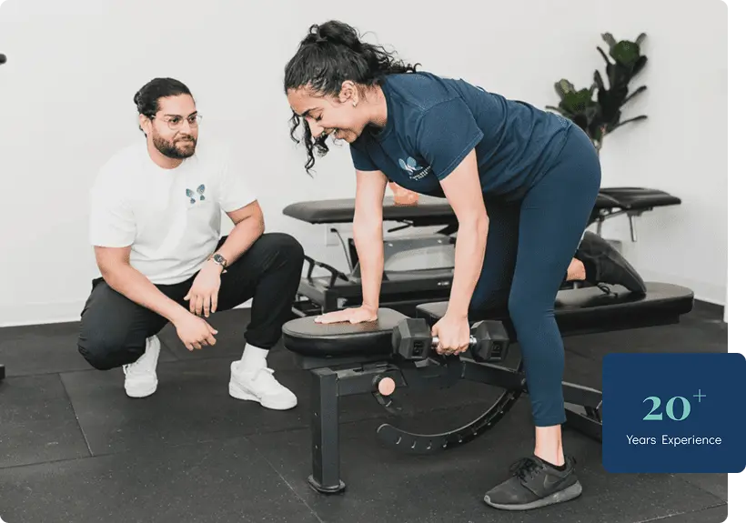 A patient performing dumbbell press on a bench & the trainer looking at her in Vancouver, Surrey & Langley