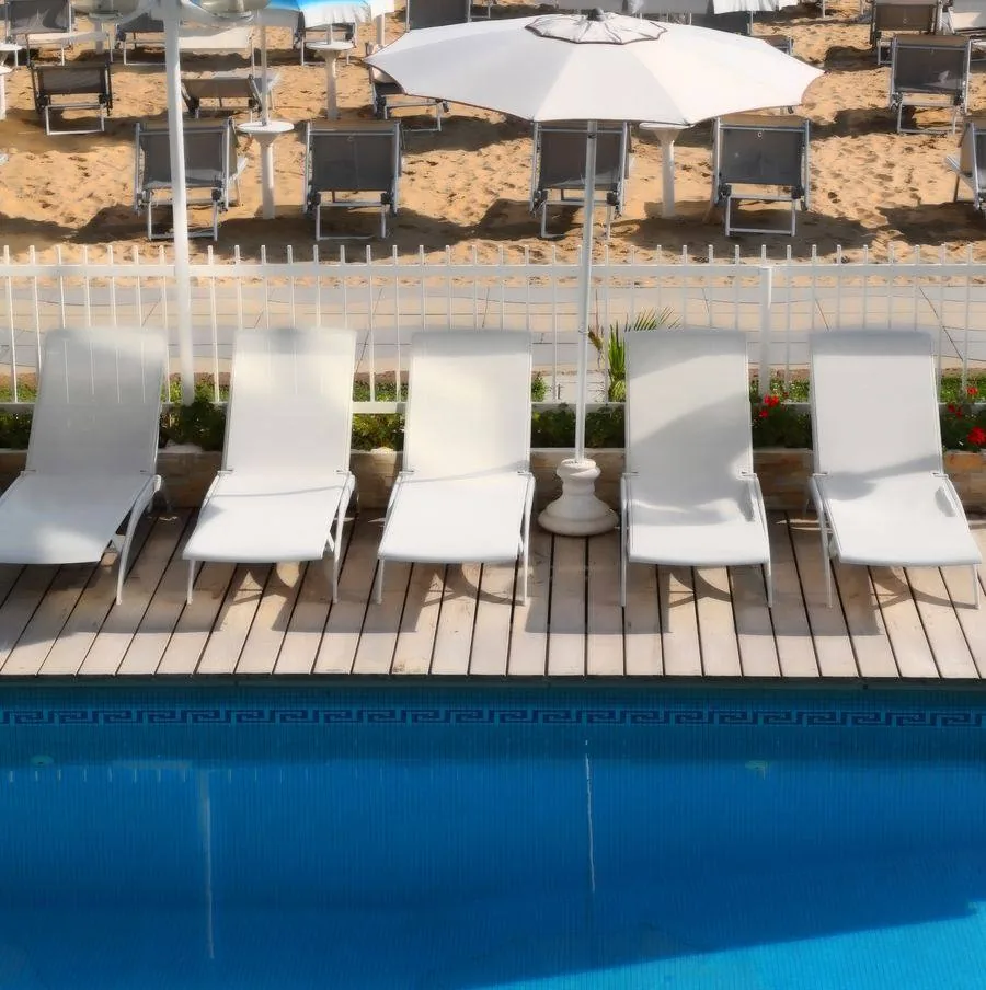 Lettini a bordo piscina con la spiaggia e gli ombrelloni di Jesolo dietro