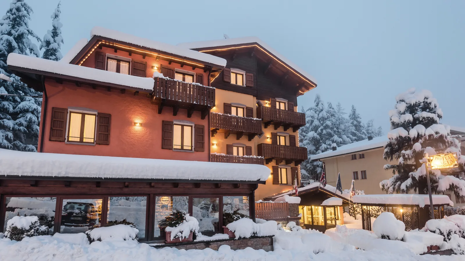 L'Hotel Pineta sotto la neve all'imbrunire, con le finestre accese e gli abeti imbiancati