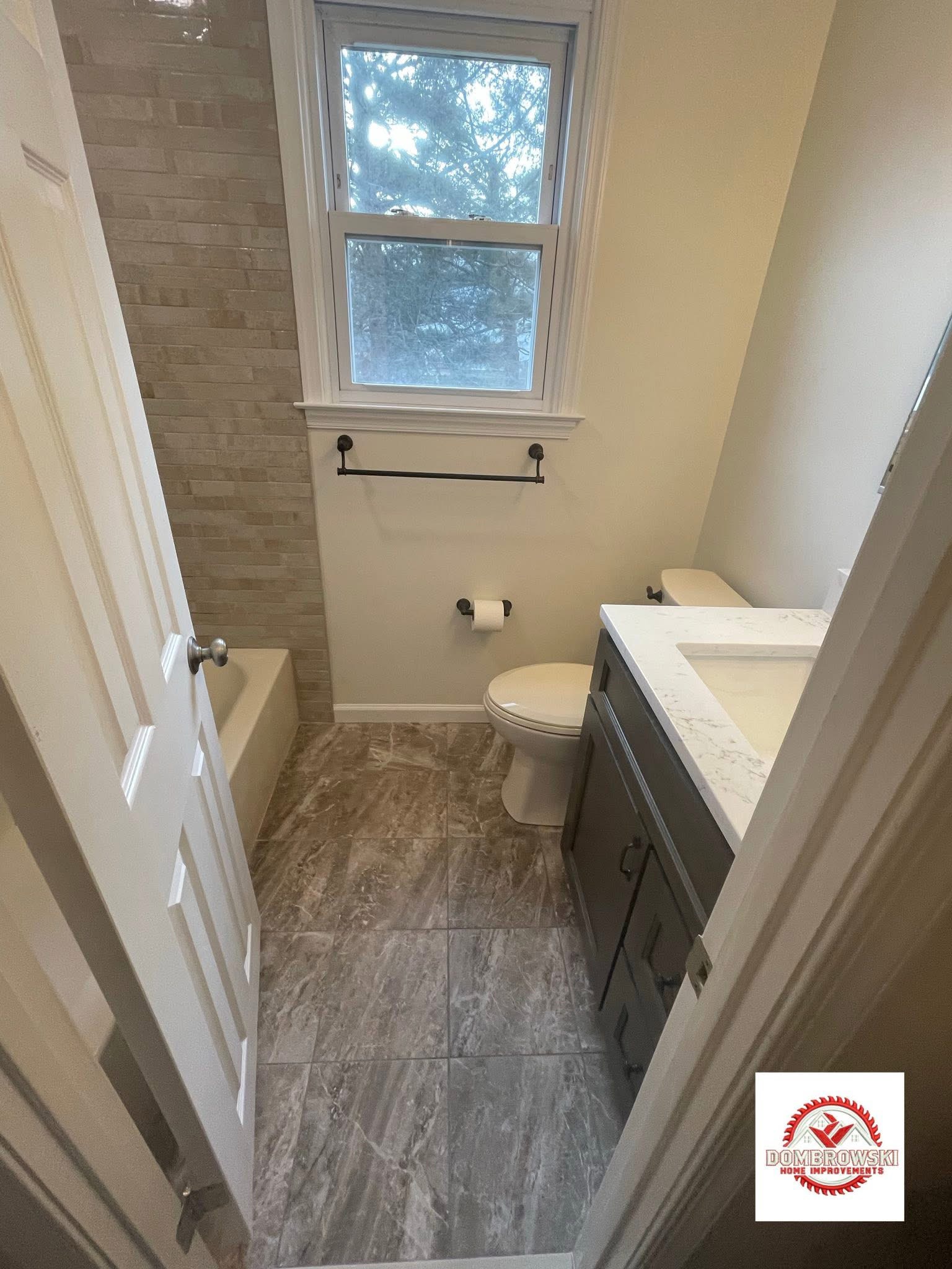 Bathroom entry view: gray vanity, marble tile floor and brick tile shower surround