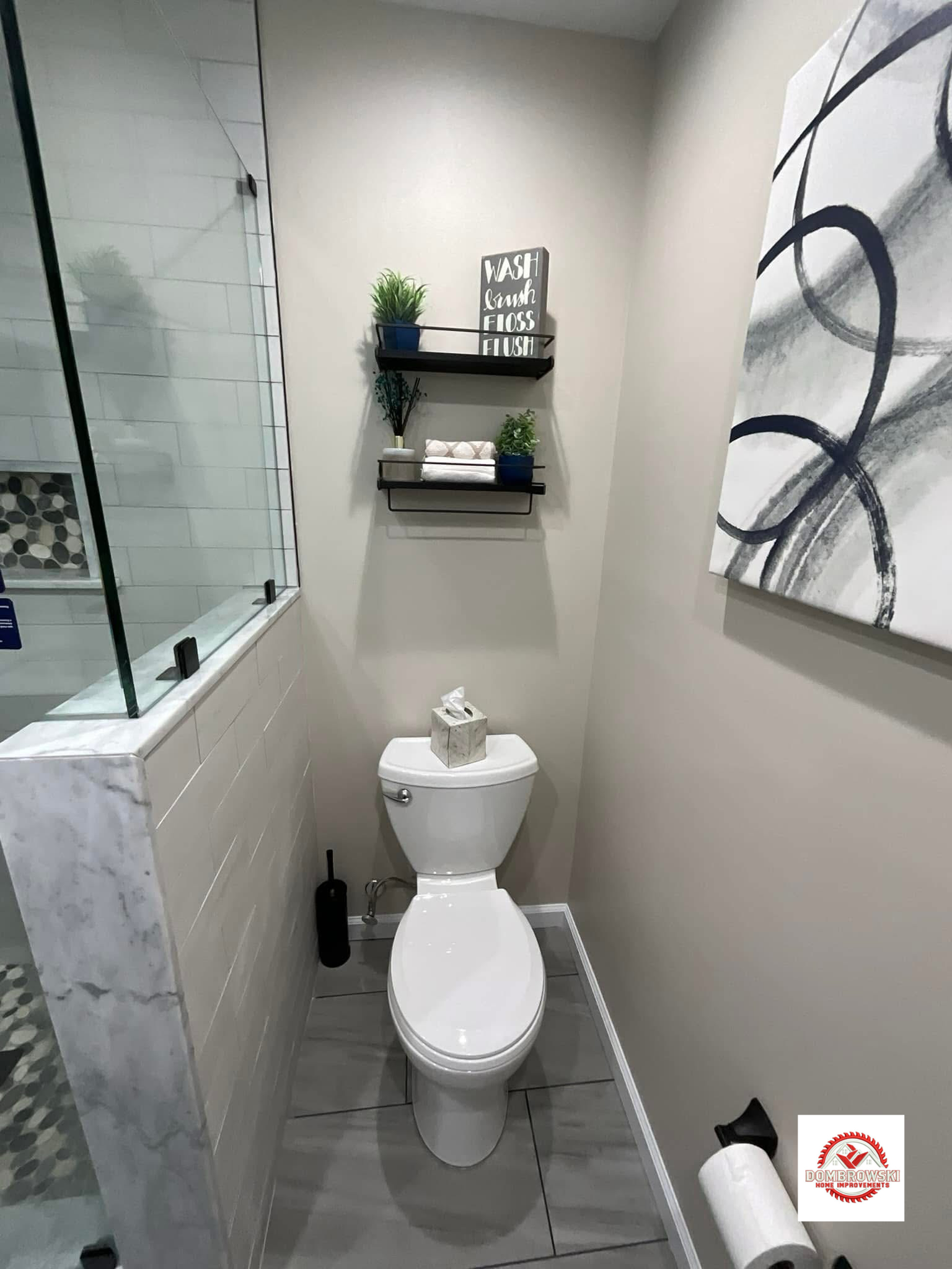 Bathroom toilet area with floating shelves, art and neutral tile floor
