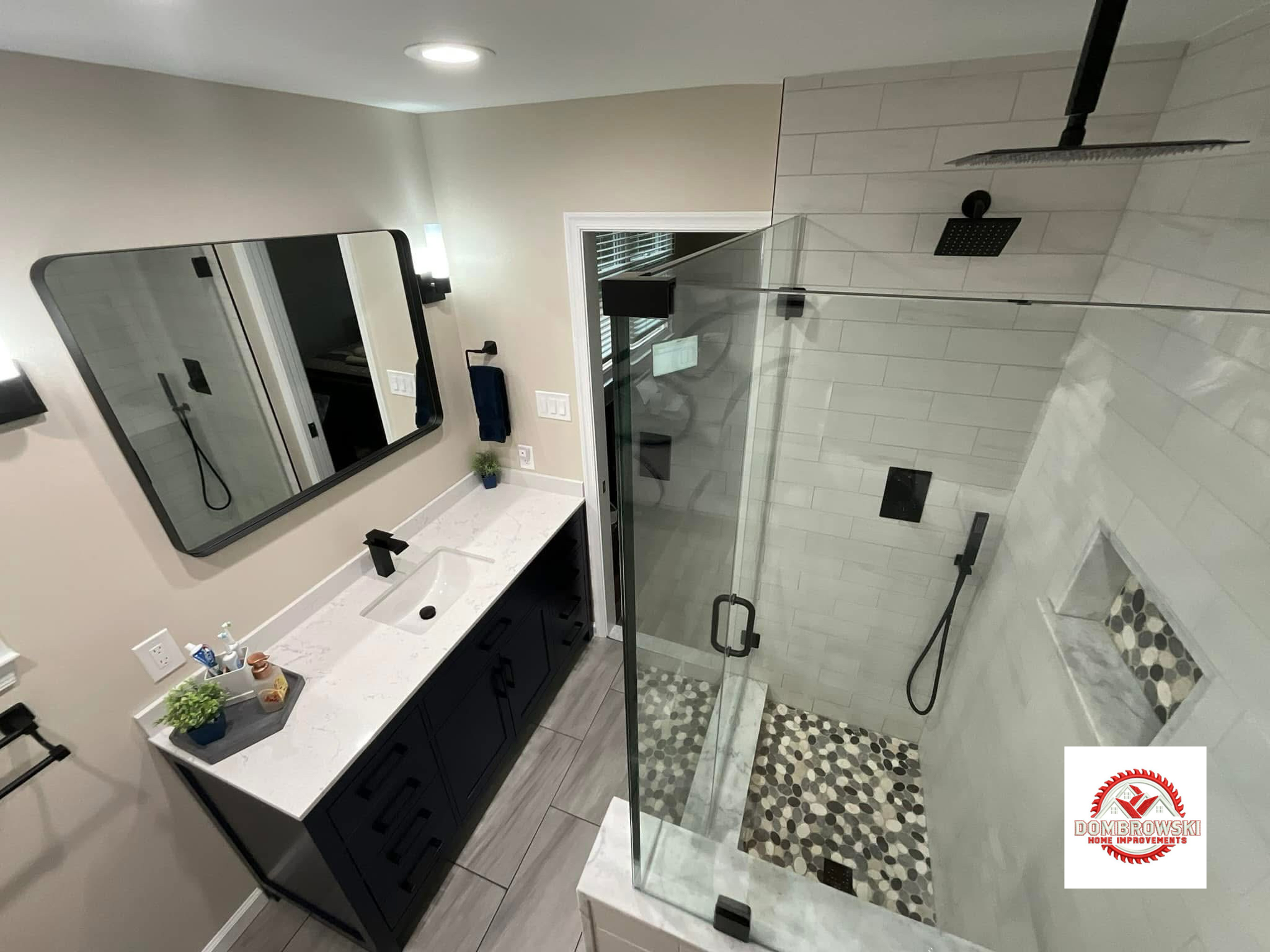 Black vanity with quartz top alongside frameless glass walk-in shower