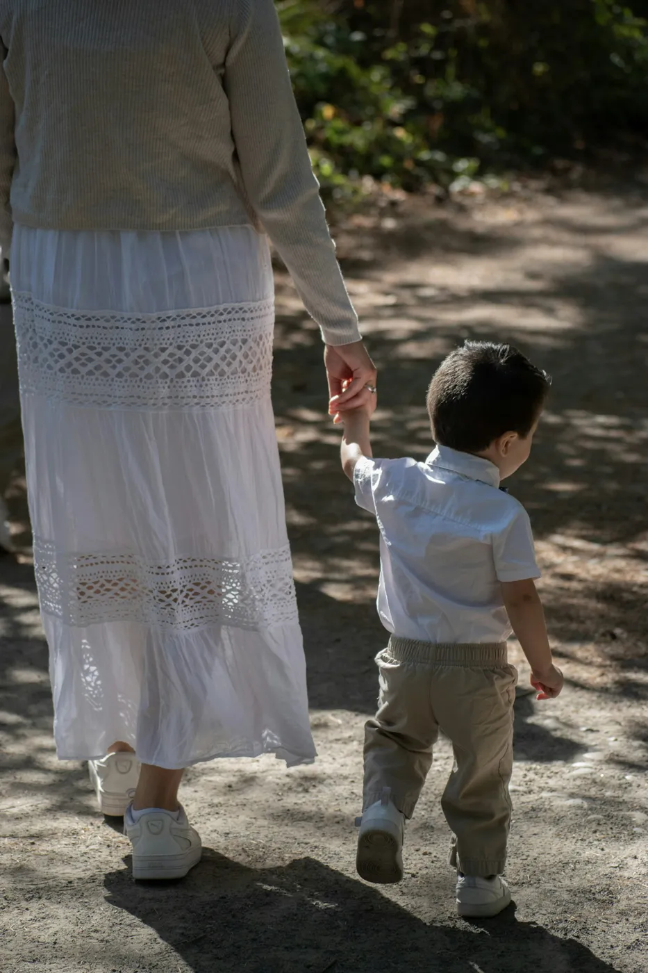 A parent and young child walking hand in hand on a sunlit path