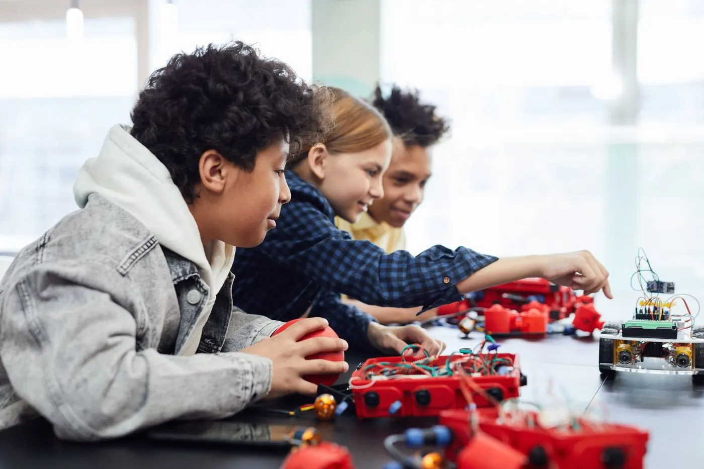 Three smiling students building a robot together with hands-on kits at a classroom table