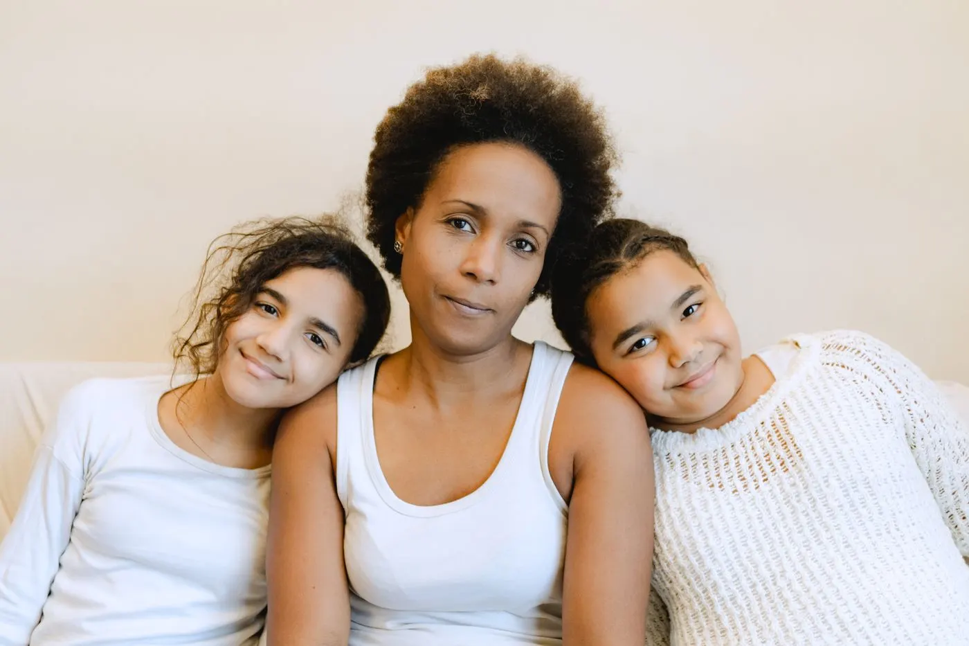 A mother at home with her two preteen daughters resting their heads on her shoulders, all three smiling