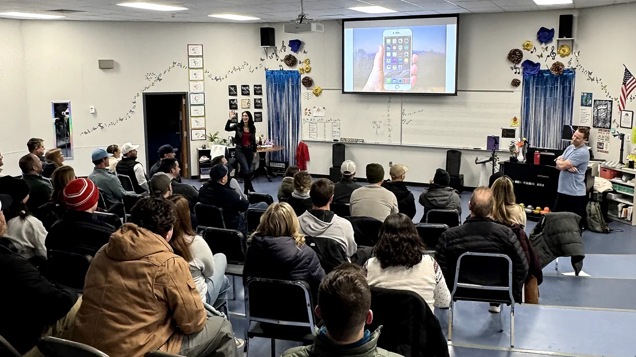 Megan presenting to a room of seated parents while Nick watches from the back
