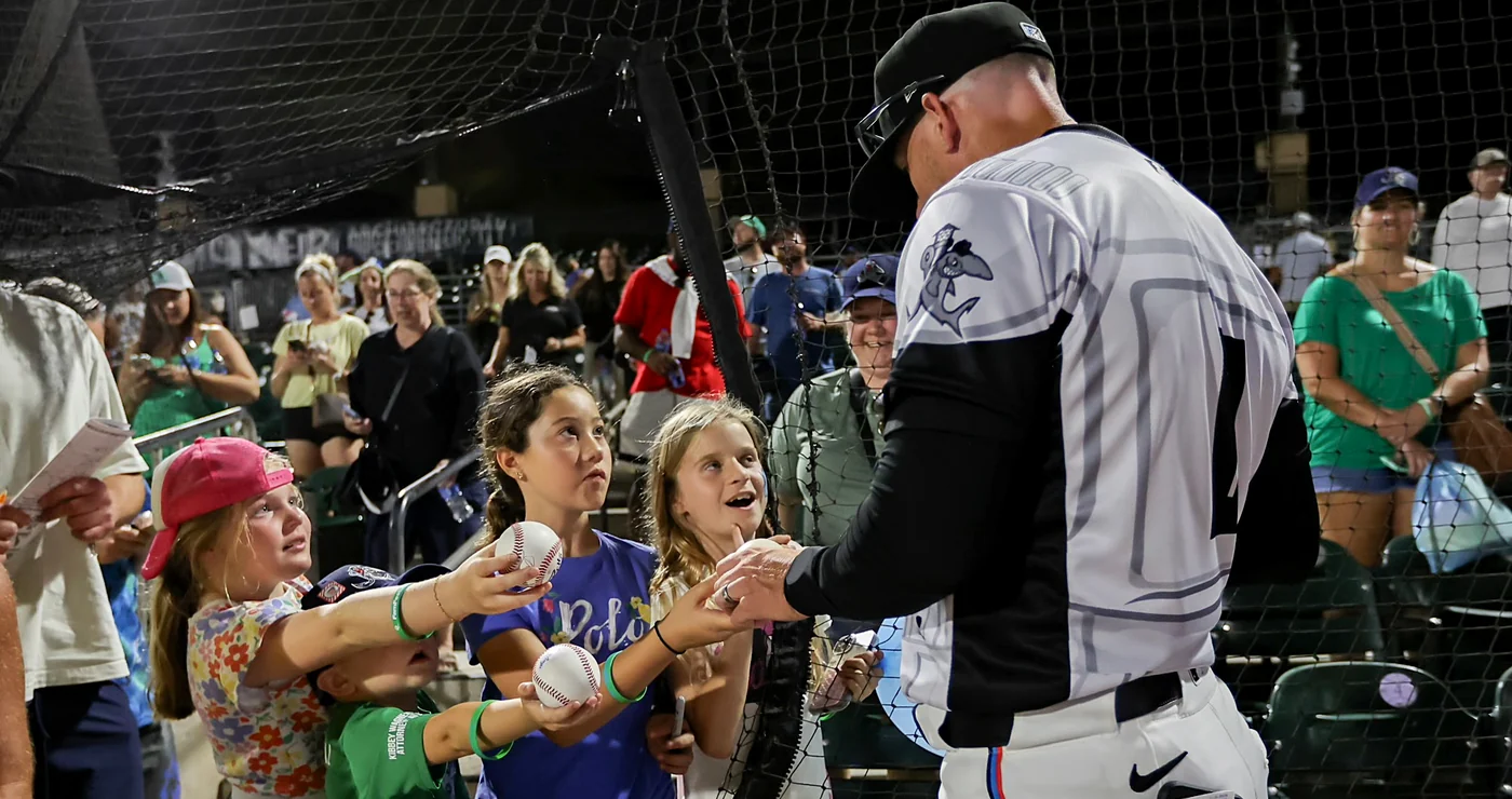 A player signing baseballs for young fans along the netting after a night game