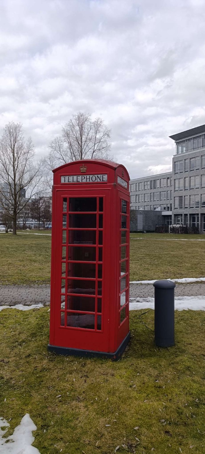 Rote britische Telefonzelle vor modernem Gebäude in Hannover – Moment zwischen Fortbildung und Alltag.
