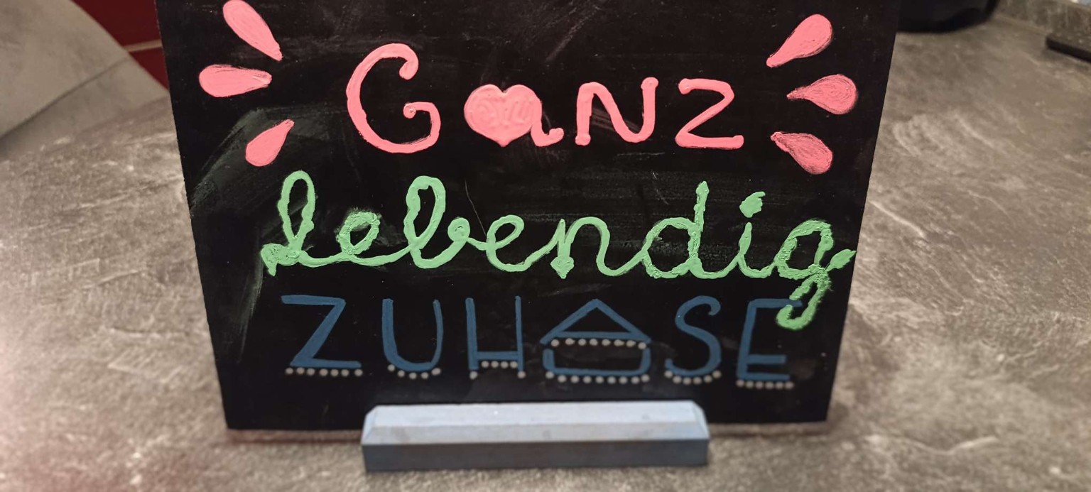 Schwarze Kreidetafel mit farbigem Lettering „GANZ. Lebendig. Zuhause.“ – persönliches Motto nach einer intensiven Zeit.