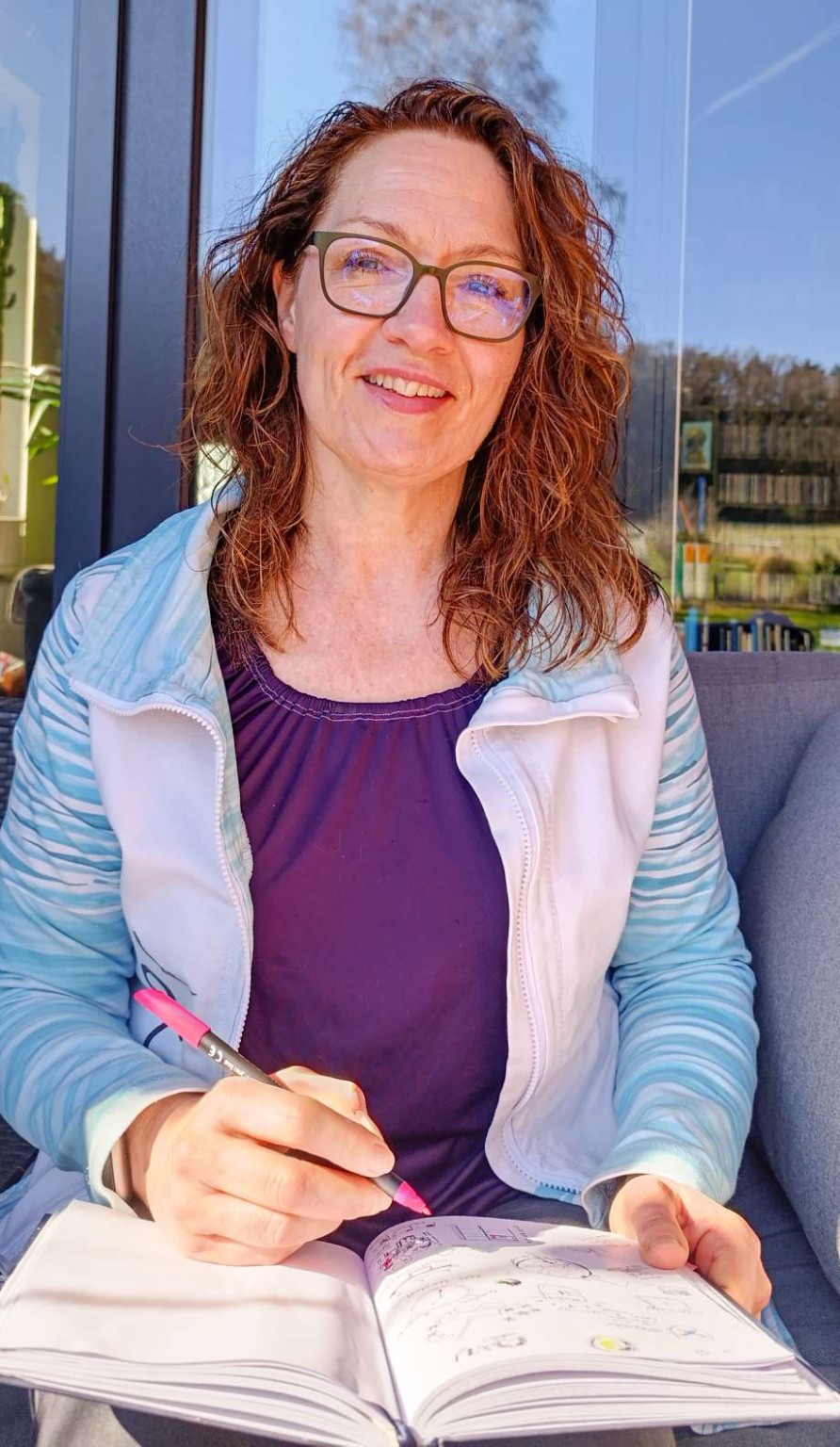 Katja Schoonbergen sitzt draußen in der Sonne und schreibt in ein Journal – kreative Auszeit, achtsames Journaling und Coaching im Moment der Ruhe.