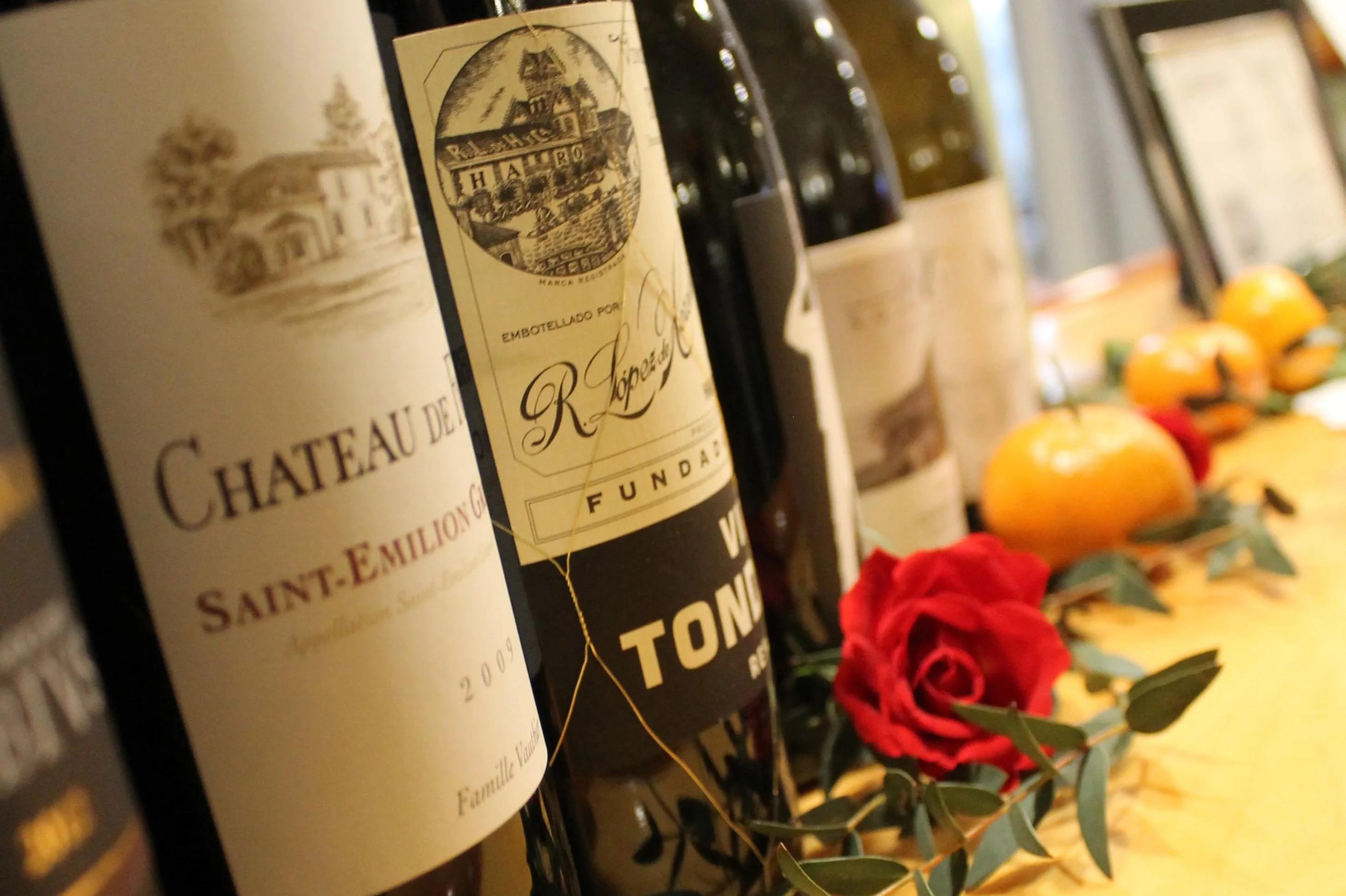 A upscale display of French red wine bottles alongside a fresh red rose, showcasing corporate event bar services and catered fundraisers.