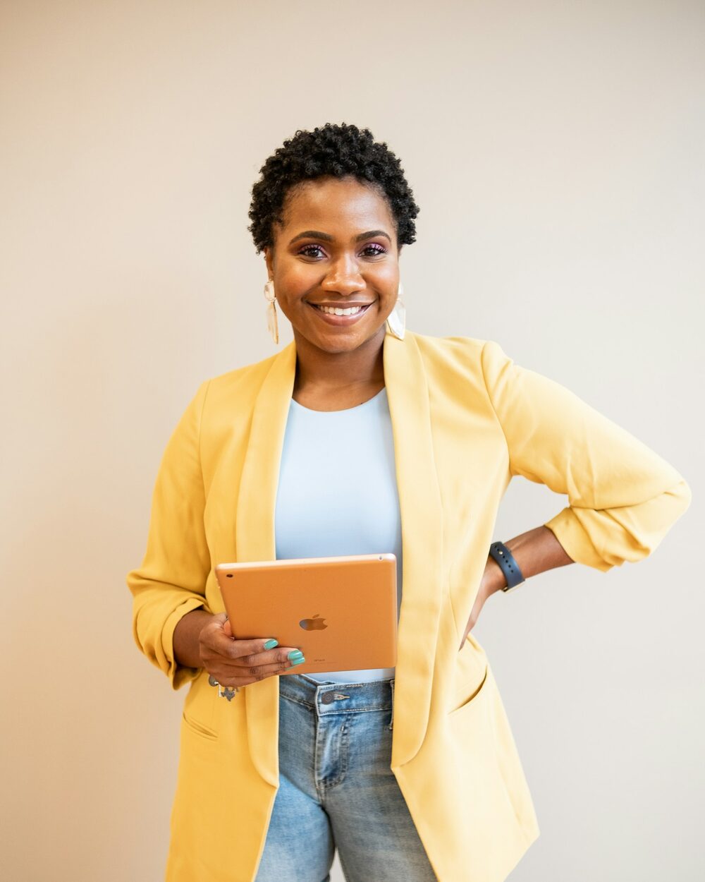 Smiling Black woman in a yellow blazer holding a tablet