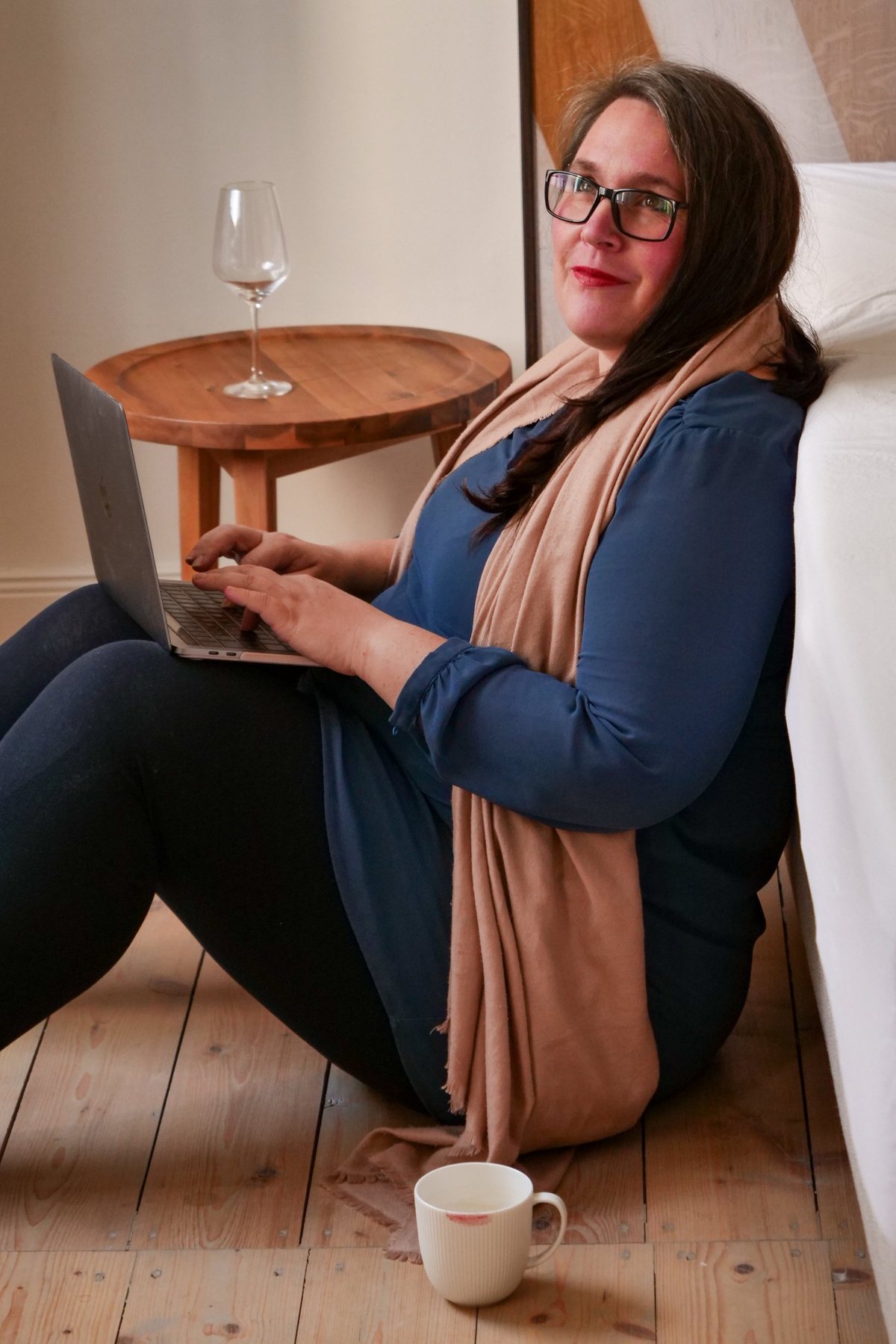 Anika Tüngerthal sitzt mit Laptop auf dem Holzboden und lächelt in die Kamera – Marketing-Mentorin für Coaches und Heilerinnen