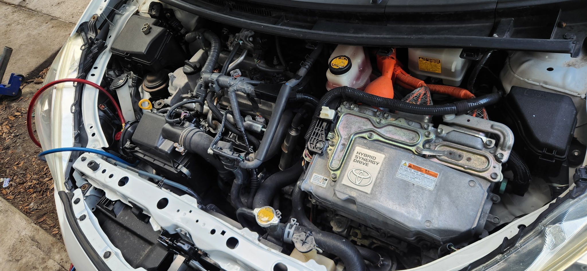 Toyota Prius hybrid engine bay with red and blue A/C service hoses connected.