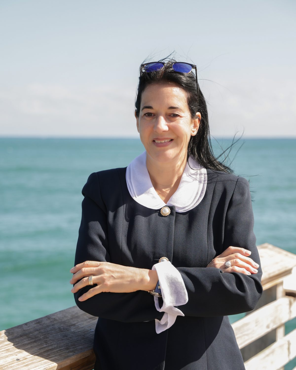 Annette Knecht Seier on a pier by the ocean, arms crossed, smiling at the camera.