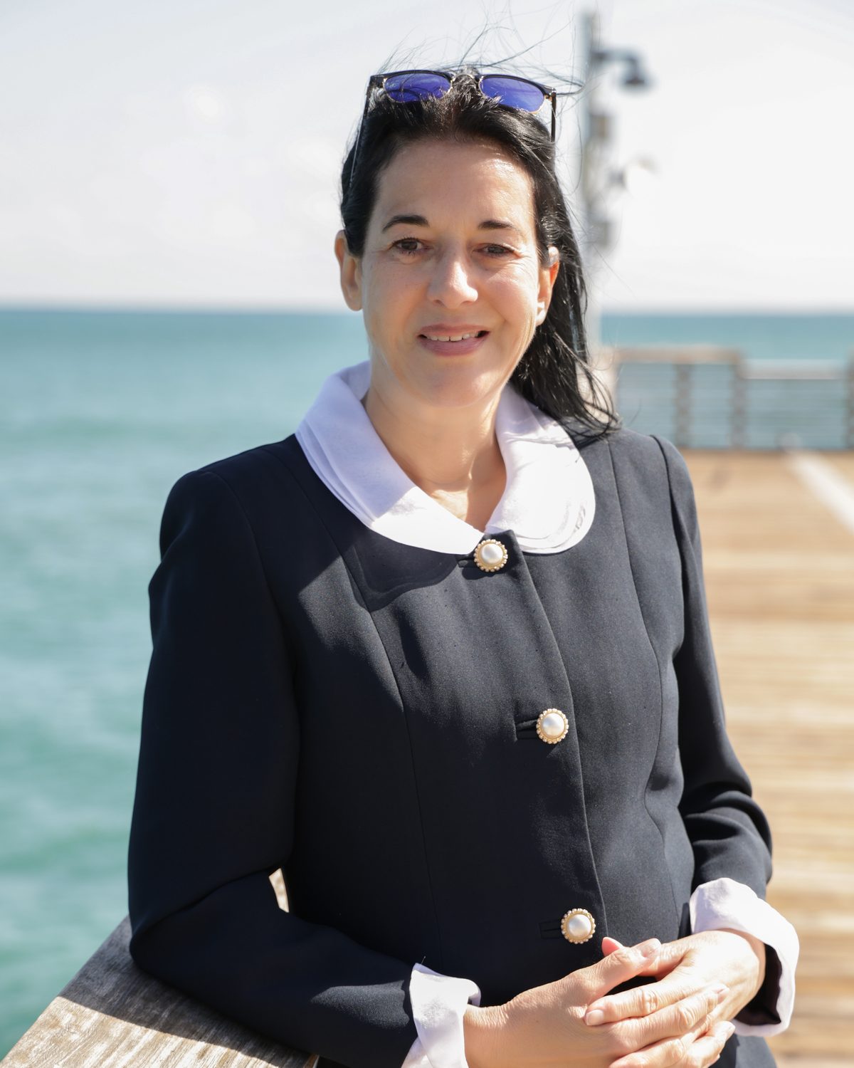 Annette Knecht Seier on a pier by the ocean, hands folded, smiling at the camera.
