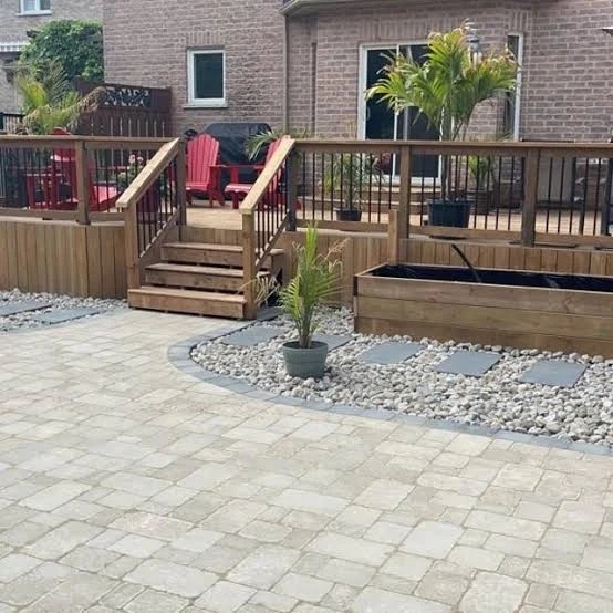 Interlocking stone patio with deck stairs and a landscaped garden edge