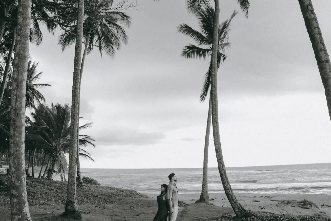 Los novios espalda con espalda entre palmeras frente al mar