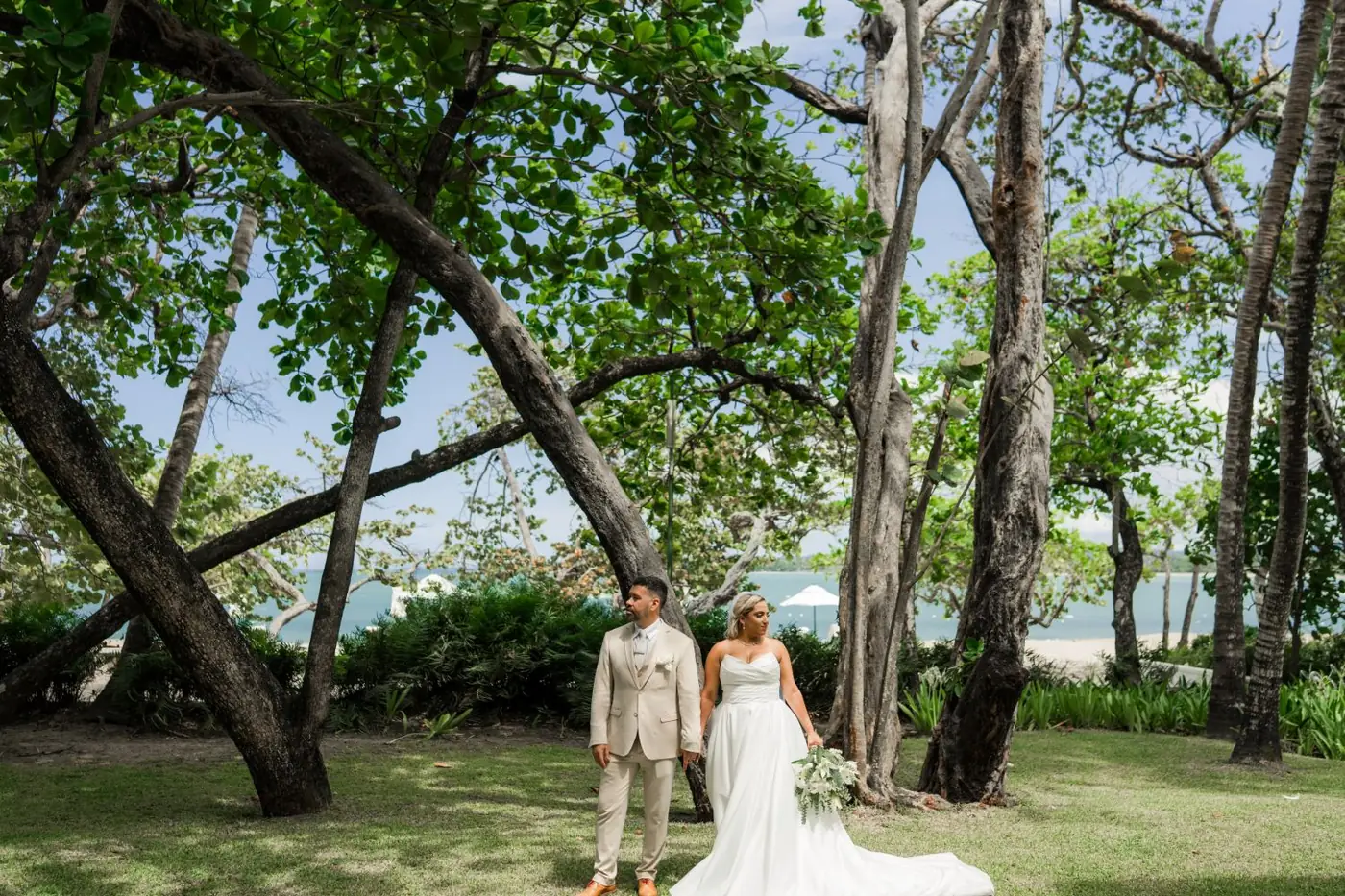 Los novios de pie entre &aacute;rboles torcidos con el mar al fondo