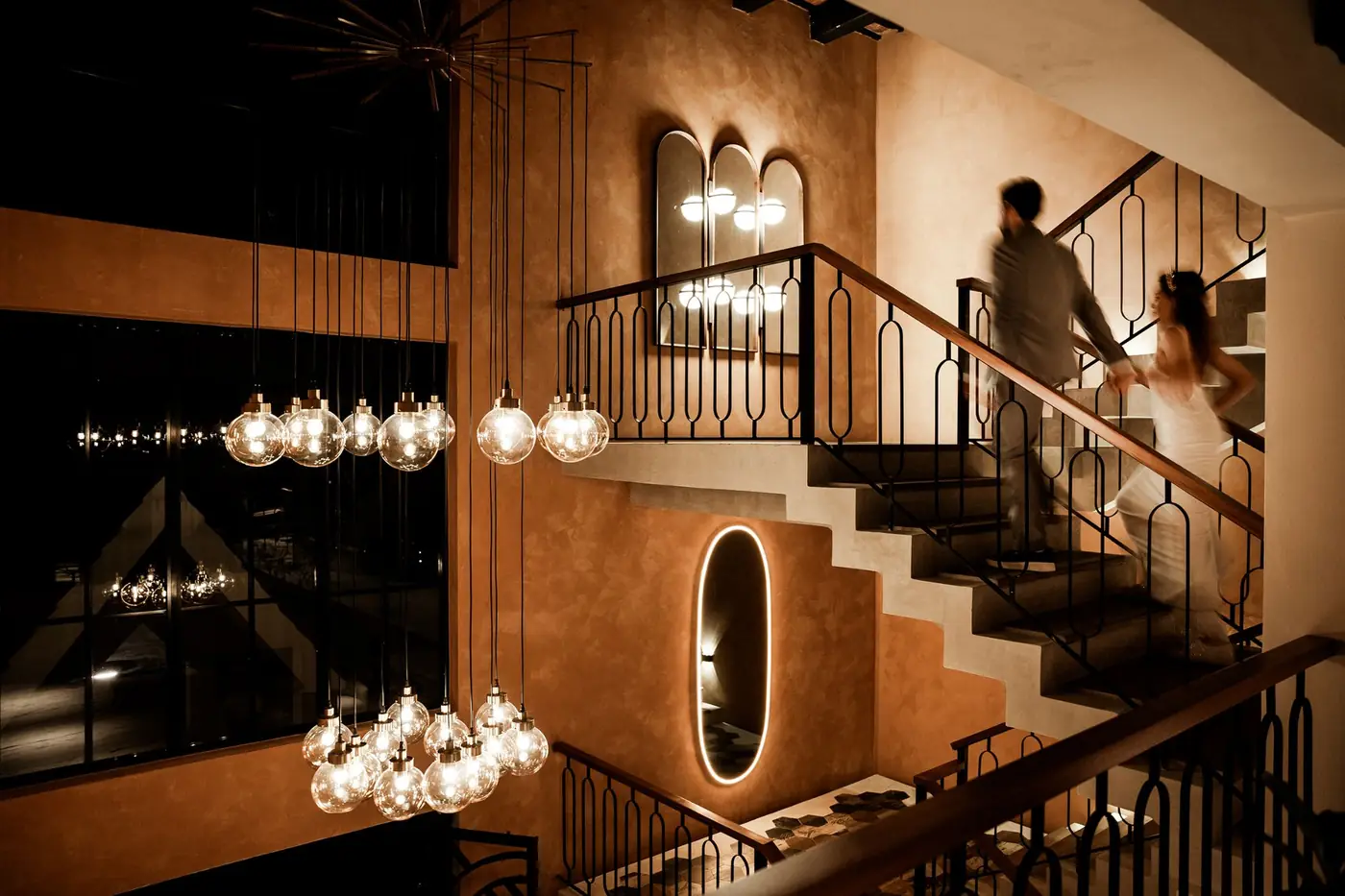 Los novios suben de la mano una escalera iluminada por l&aacute;mparas colgantes