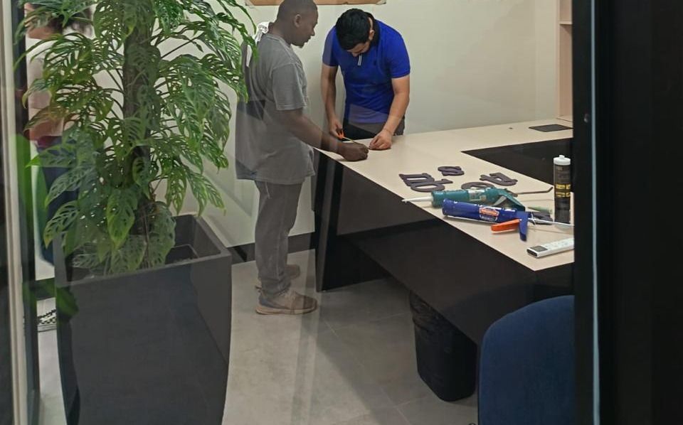 Operarios midiendo y colocando letras corpóreas sobre la barra de una sala de reuniones