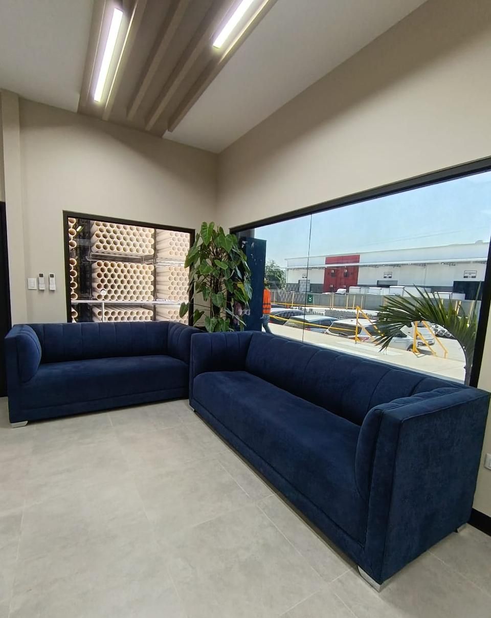 Sala de espera con ventanal a doble altura, dos sofás azules y vitrina de producto al fondo