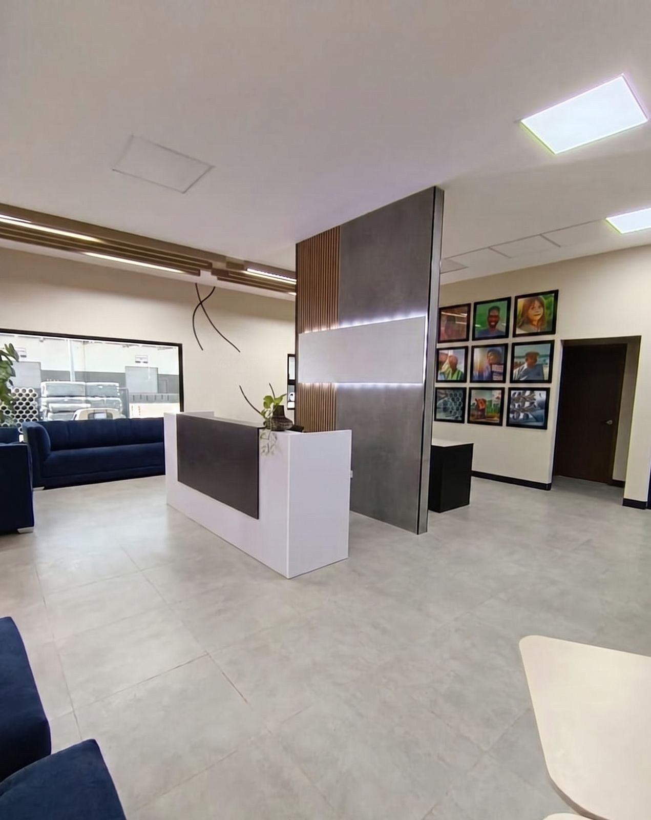Recepción corporativa con mostrador blanco al centro, sala de espera con sofás azules y galería fotográfica