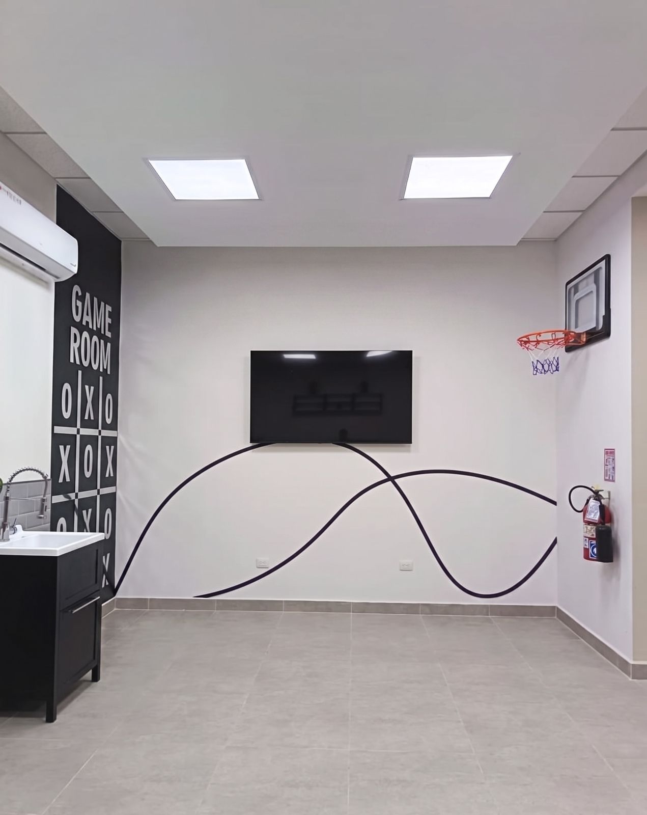 Sala de juegos con mural ilustrado, aro de basket y pantalla, muro blanco con grafismo ondulado