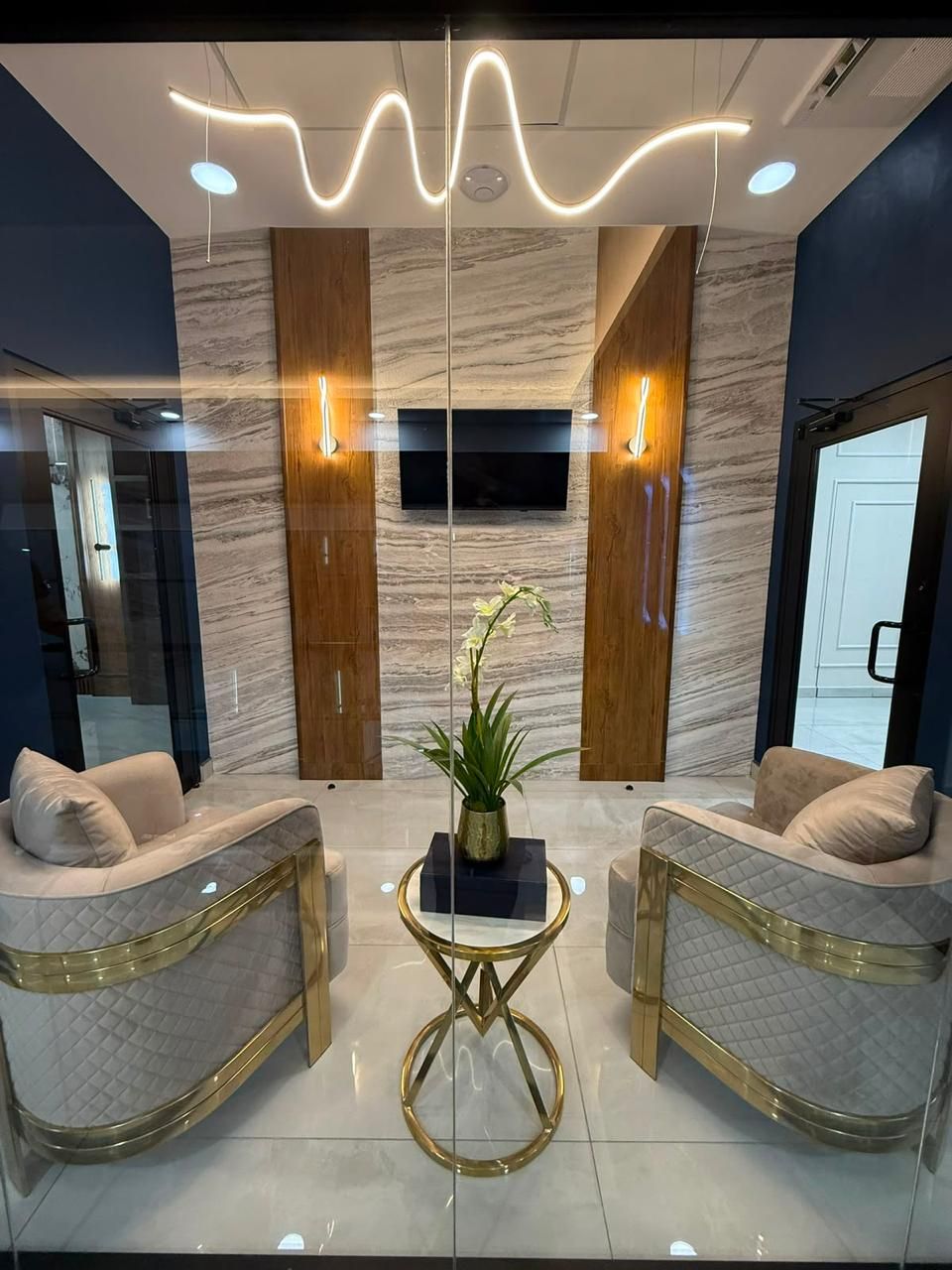 Lobby de travertino con lámpara lineal ondulada, sillones dorados y mesa auxiliar de latón